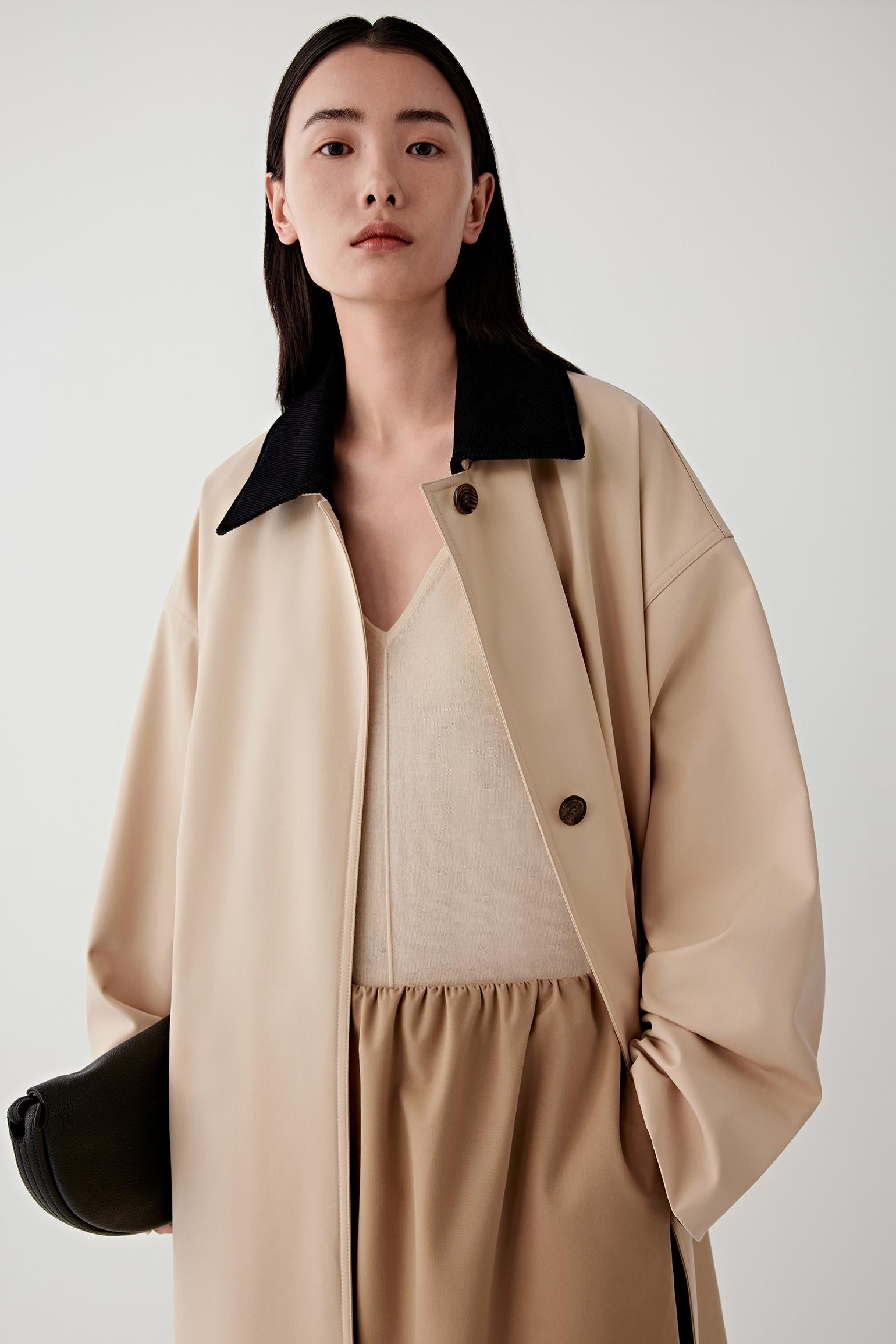 Woman wearing a beige coat with a black collar against a white background