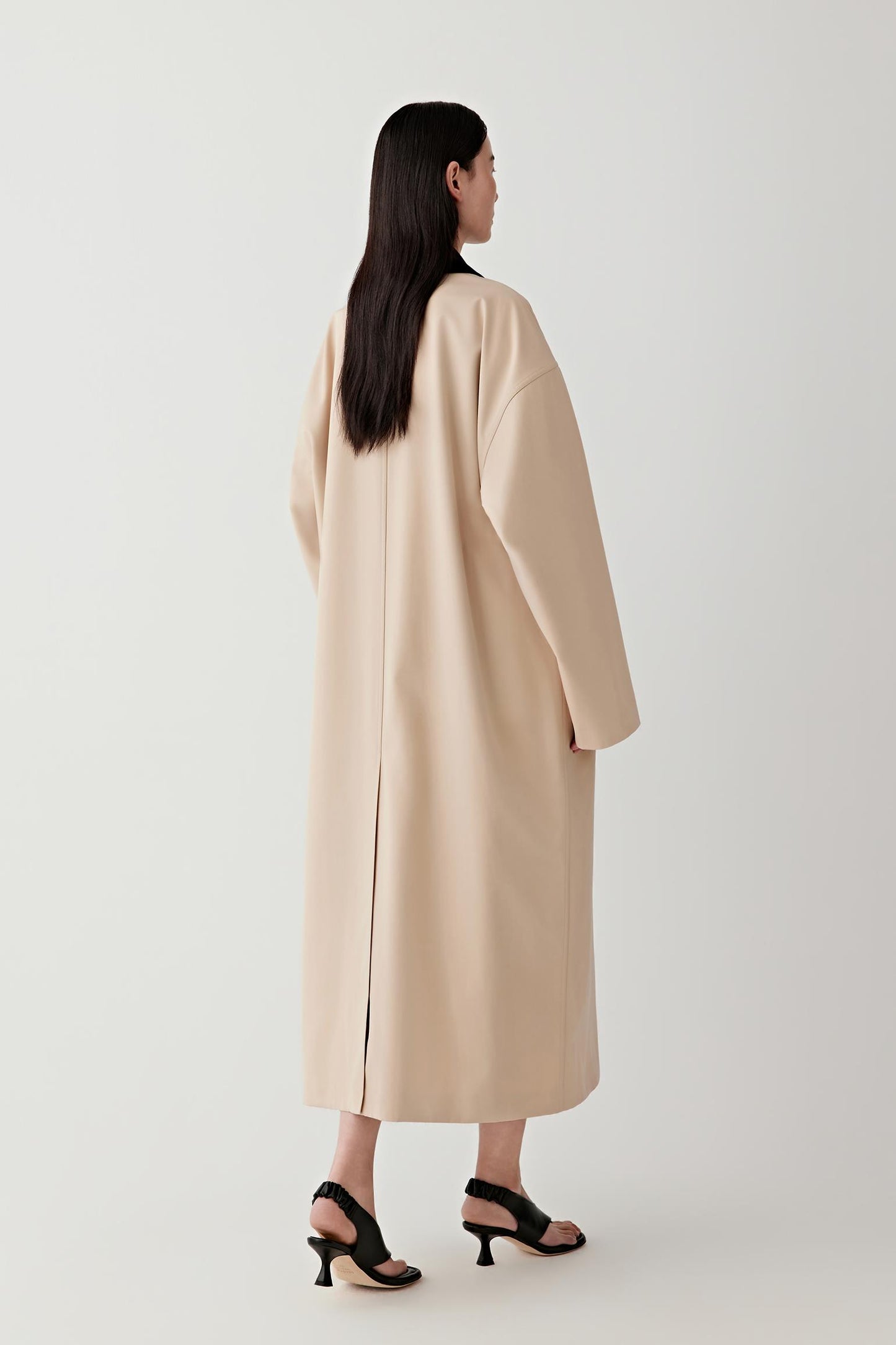 Woman wearing a beige coat standing against a white background