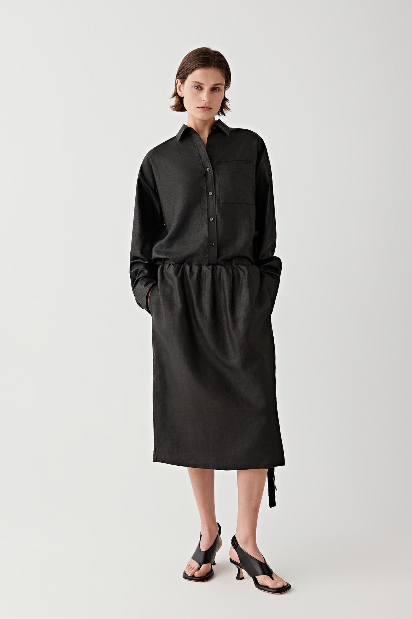 Full-length front view showing the midi-length silhouette and softly gathered waist construction. The elasticated waistband creates gentle volume while allowing the skirt to fall in a continuous fluid line through the body.