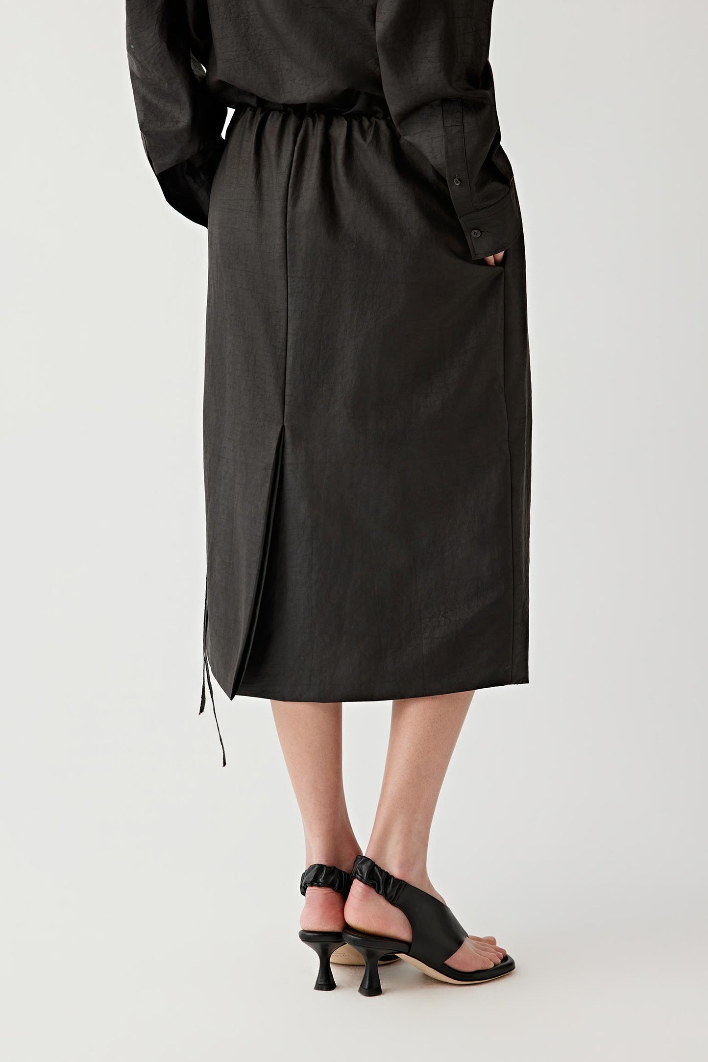 Side view emphasizing the movement and fluidity of the skirt. The lightweight silk construction follows the body softly while maintaining a clean silhouette and subtle structure through the hemline.