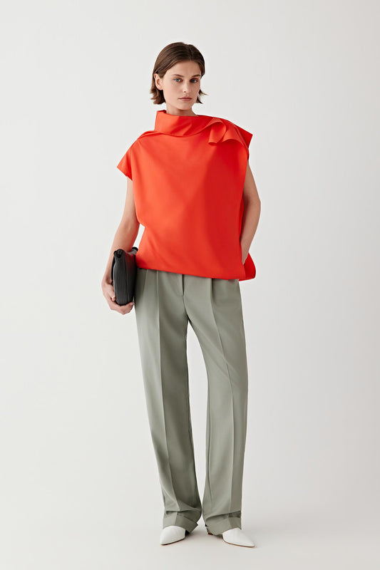Full-length front view showing the blouse paired with tailored trousers, emphasizing the gently draped collar and fluid movement of the silk fabric
