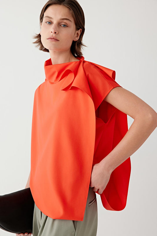Front view of a woman wearing a vivid red sleeveless blouse in spun silk, highlighting the fluid drape, soft surface and lightly structured silhouette