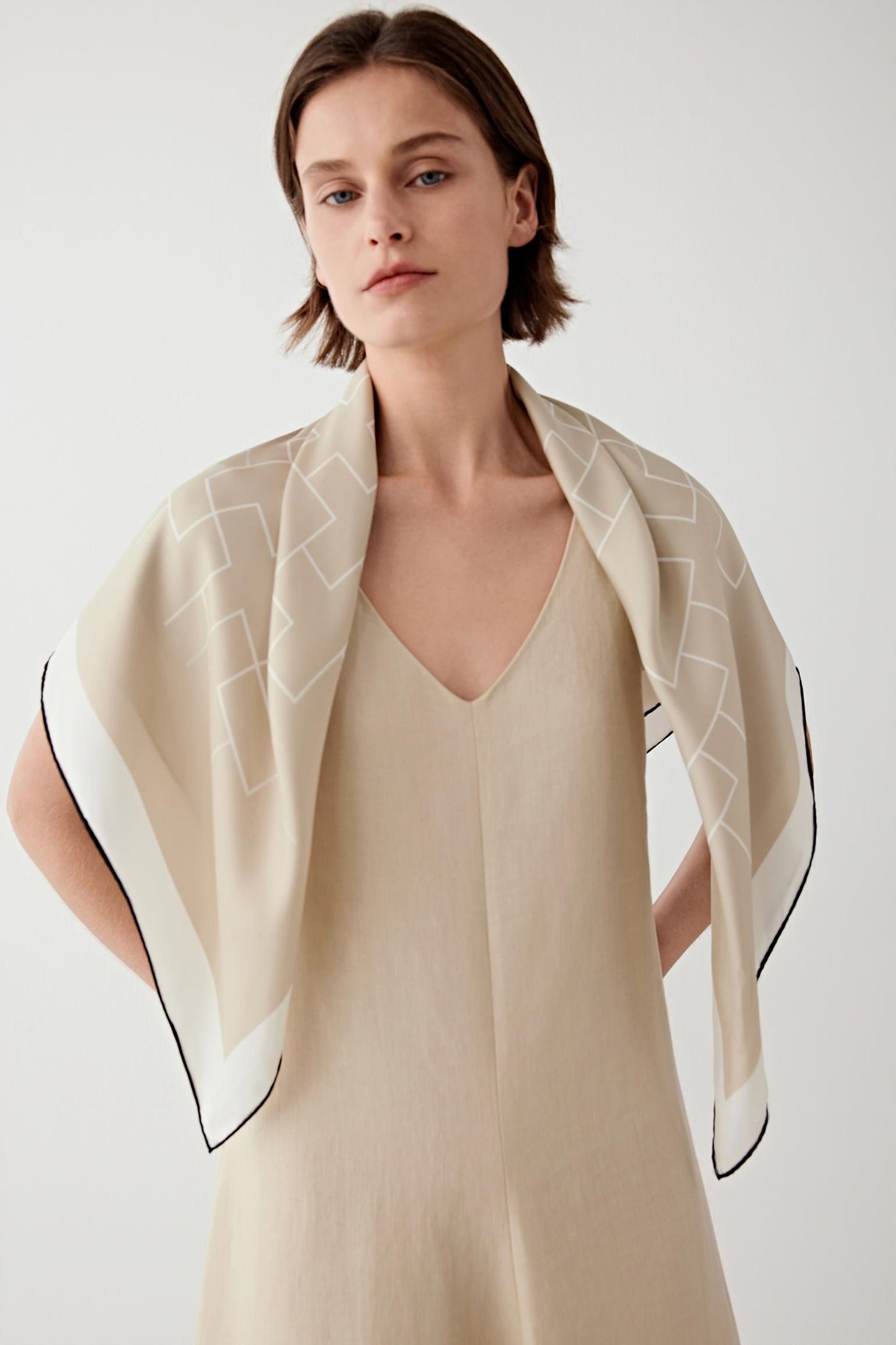 Woman wearing a soft beige silk twill scarf draped over the shoulders.