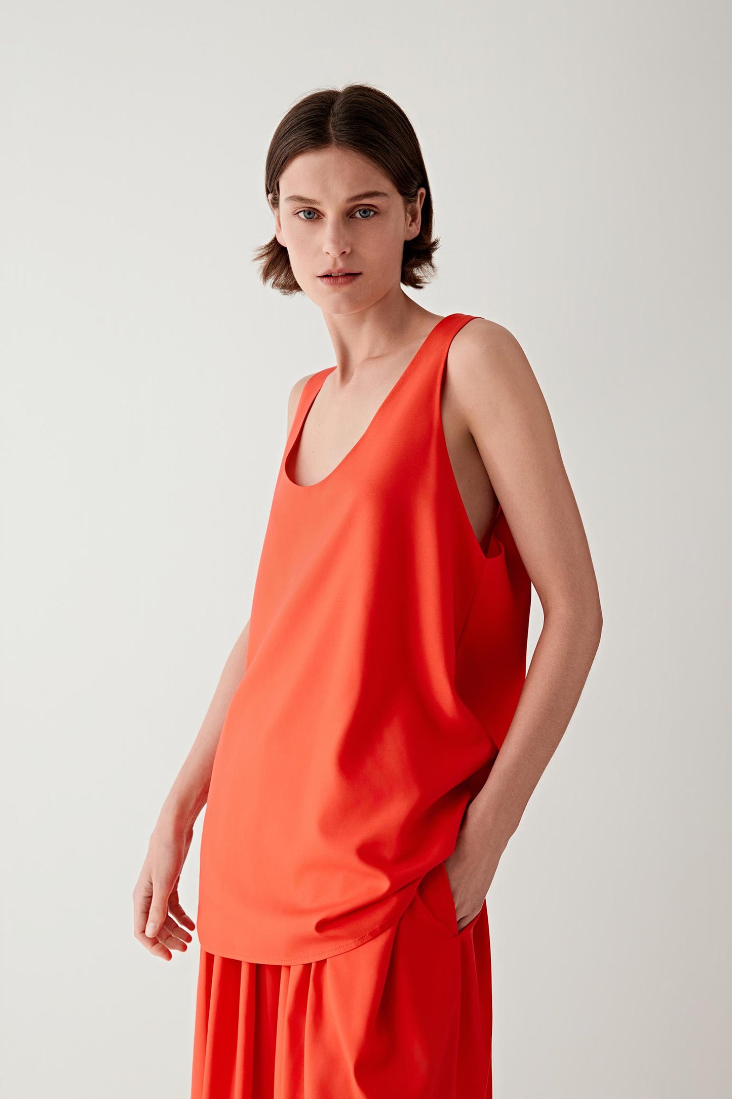 Front view of a woman wearing a red sleeveless top in spun silk poplin, highlighting the smooth surface, lightweight structure and fluid drape