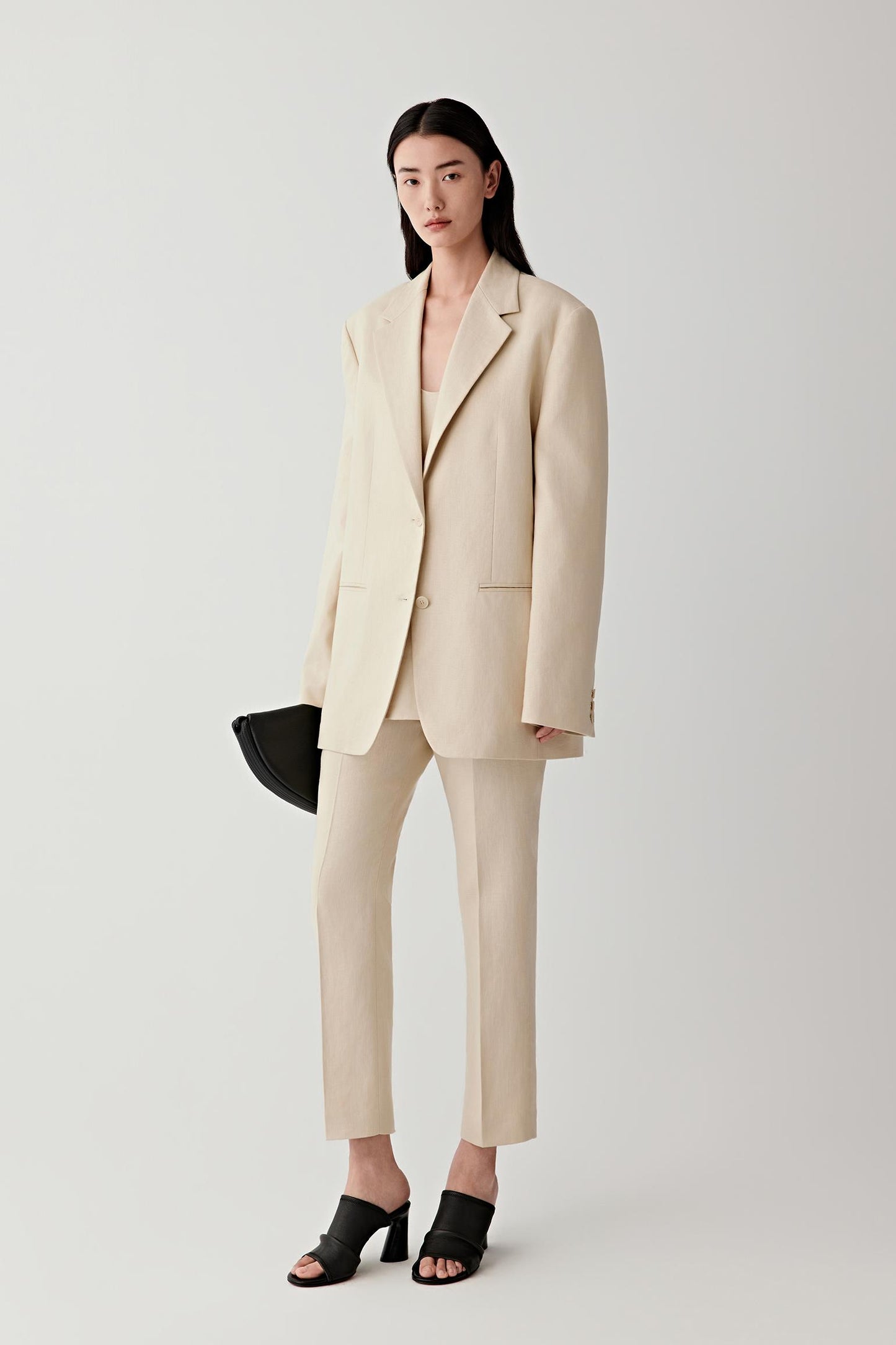 Woman wearing a nude tailored blazer with matching trousers, full-length view.