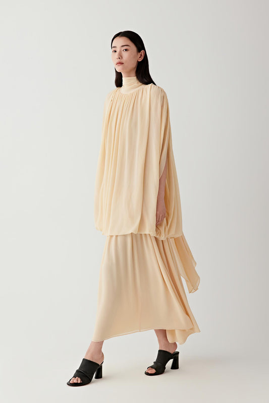 Full-length front view of a woman walking slightly forward wearing a pale lemon yellow silk georgette long dress, highlighting the elongated silhouette, fluid drape and softly matte, lightweight texture, with layered panels creating gentle movement along the length