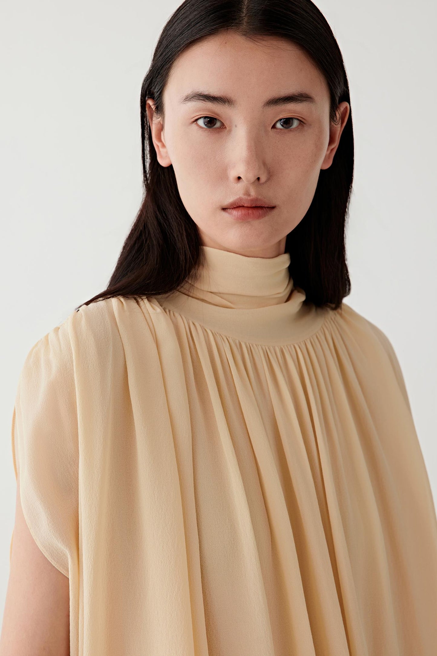 Close-up portrait focusing on the neckline and upper bodice, showing the high neckline, fine gathers and the delicate, slightly sheer texture characteristic of silk georgette