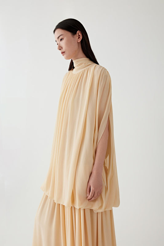 Full-length side view showing the dress in profile, emphasizing the vertical fall from high neckline to hem, the airy construction of the fabric and the way the layered structure moves fluidly with the body