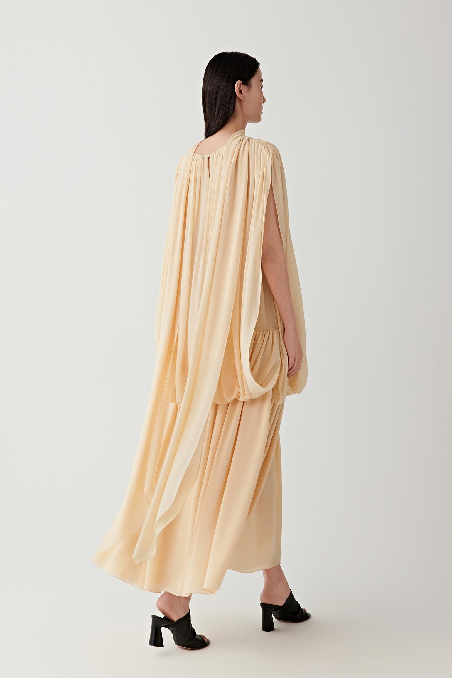 Full-length back view highlighting the gathered construction at the upper back, the continuous flow of the fabric and the elongated, softly expanding silhouette toward the hem