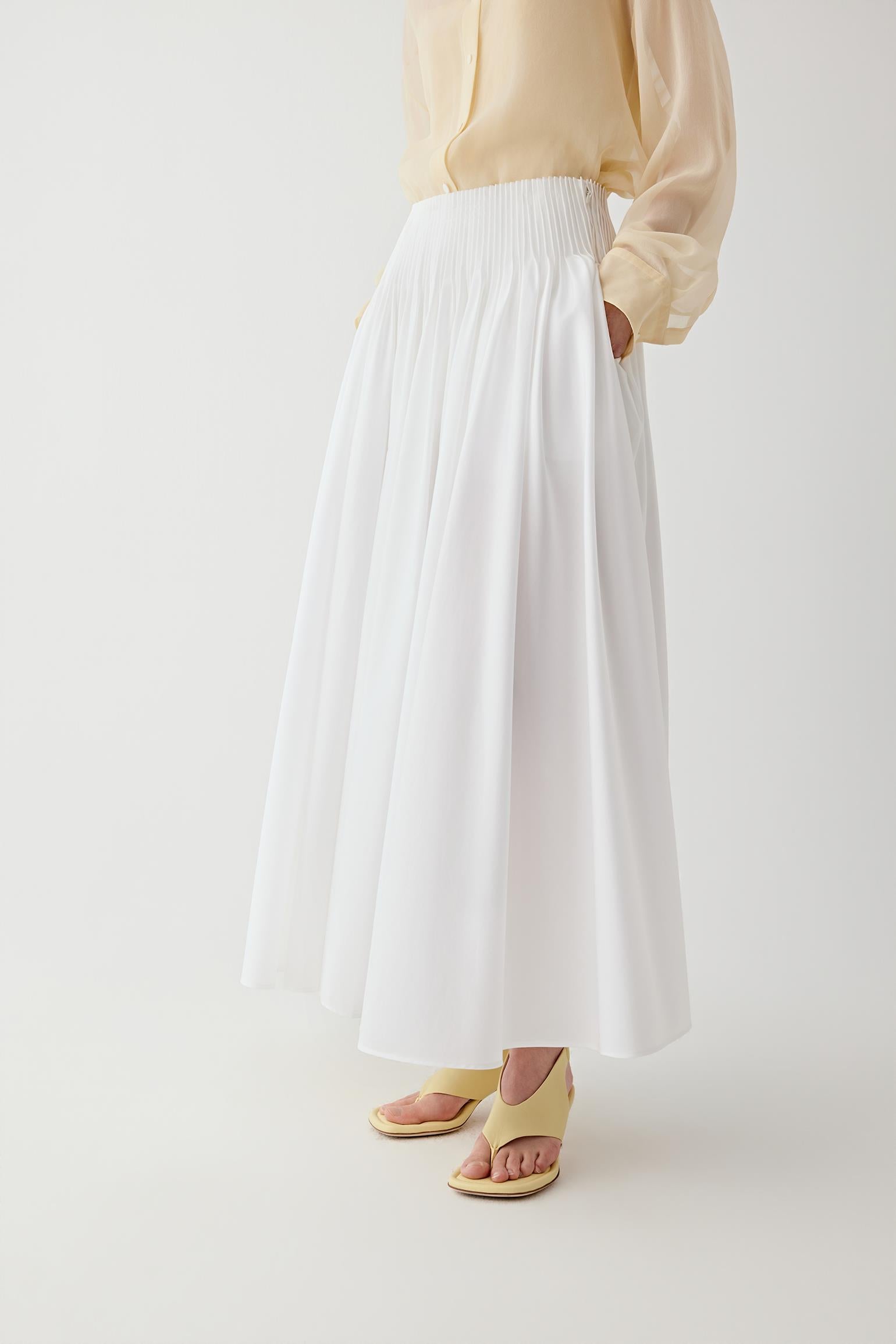 Side or three-quarter view emphasizing the movement created by the pleated construction and the continuous vertical line of the silhouette. The fabric retains a crisp appearance while allowing fluid motion.