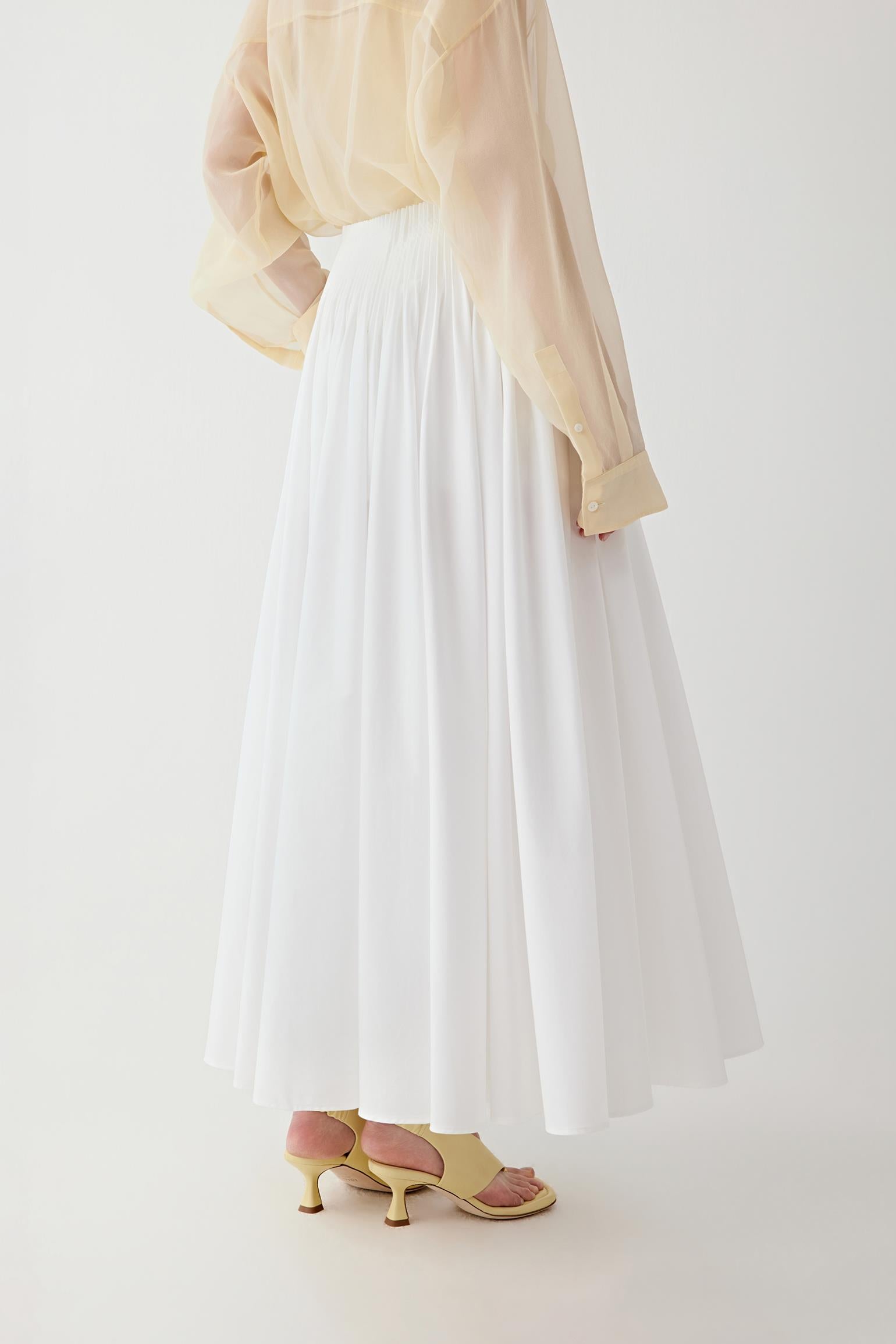Side or three-quarter view emphasizing the movement created by the pleated construction and the continuous vertical line of the silhouette. The fabric retains a crisp appearance while allowing fluid motion.