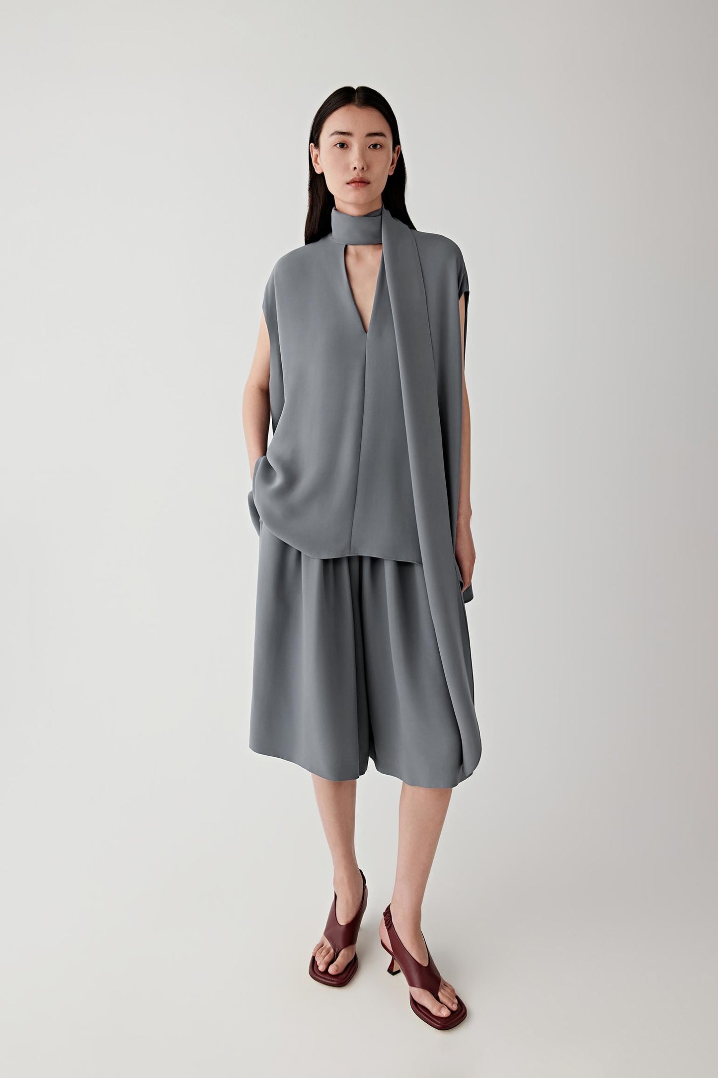 Front view of a woman wearing grey fluid shorts in silk crepe, highlighting the lightweight texture, matte surface and fluid drape of the fabric. The silk crepe falls softly while maintaining a lightly structured silhouette.