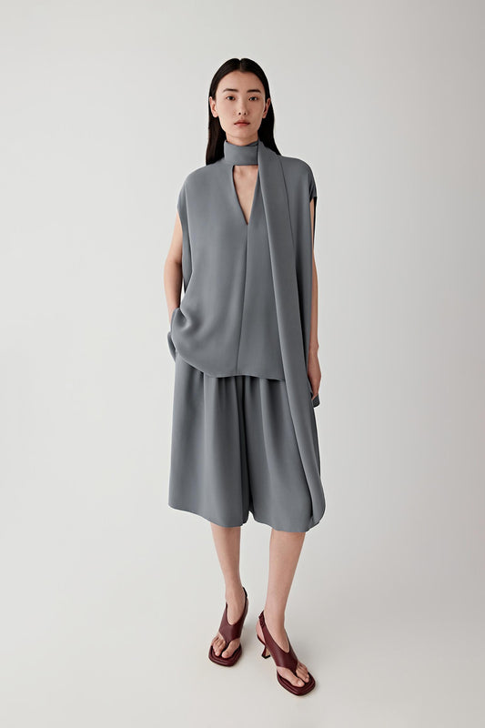 Front view of a woman wearing grey fluid shorts in silk crepe, highlighting the lightweight texture, matte surface and fluid drape of the fabric. The silk crepe falls softly while maintaining a lightly structured silhouette.