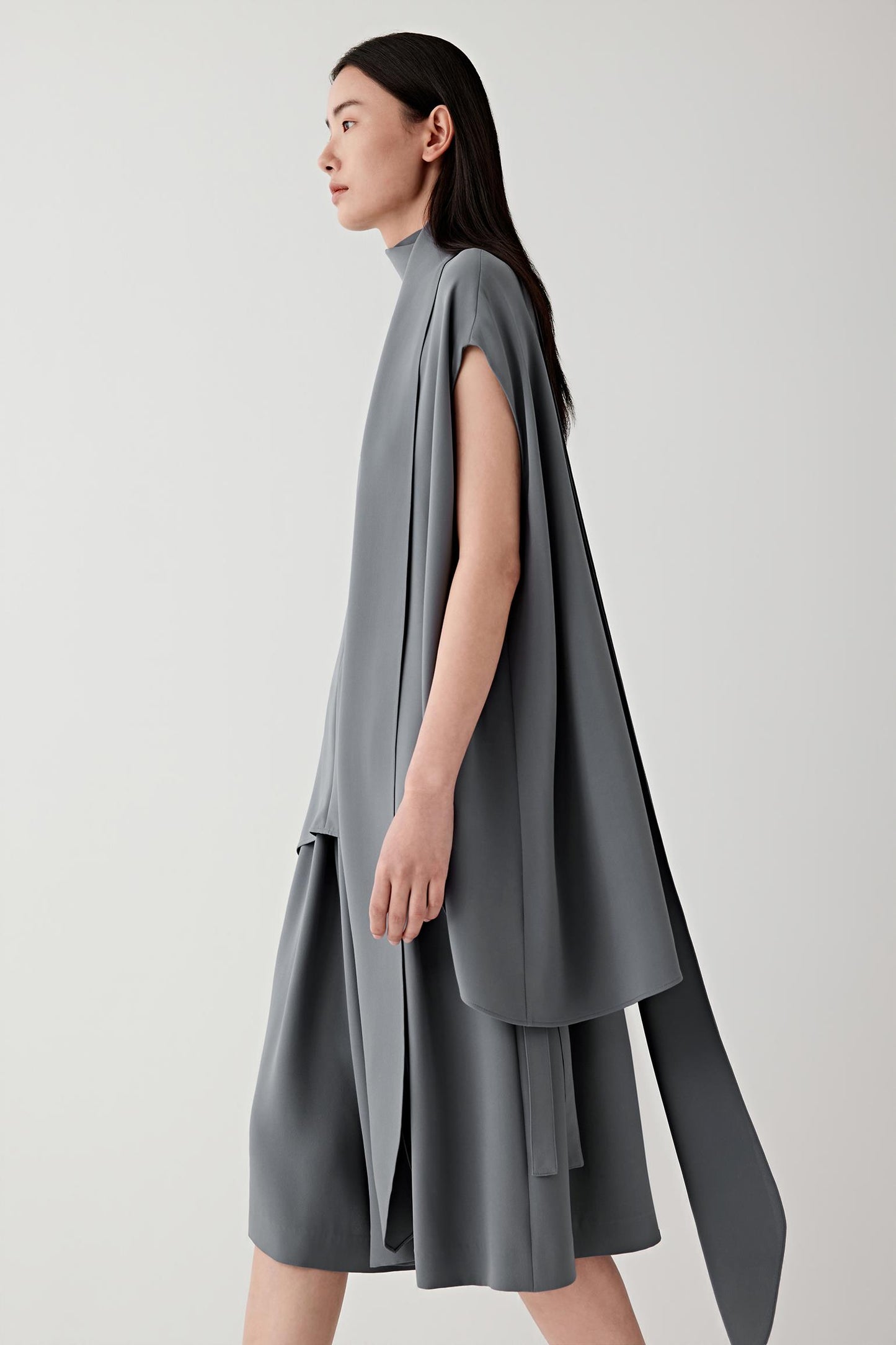 Side or three-quarter view emphasizing the layered construction and fluid drape of the heavy silk crepe. The fabric falls softly away from the body, revealing the continuous movement and balanced proportions of the silhouette.