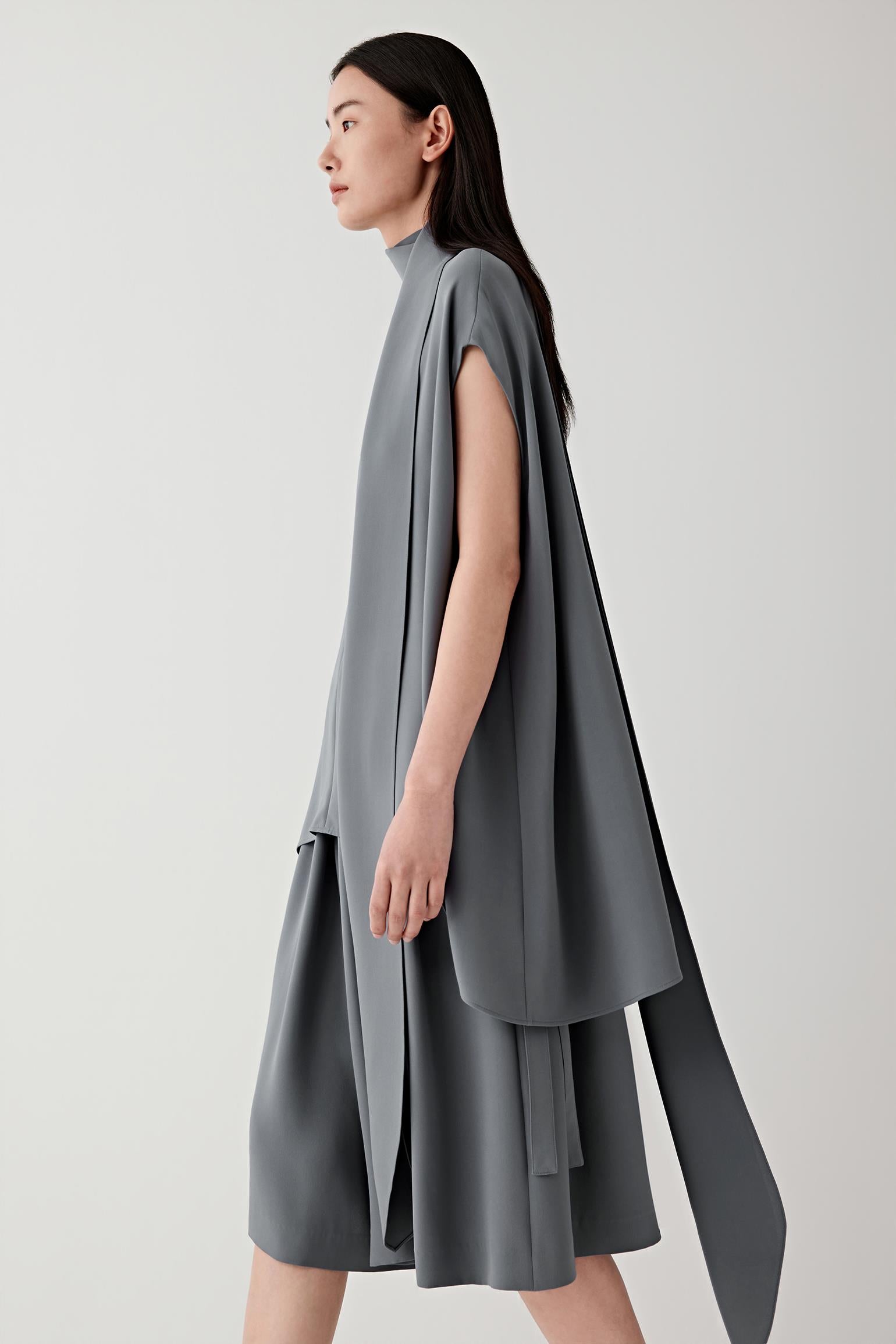 Side or three-quarter view emphasizing the layered construction and fluid drape of the heavy silk crepe. The fabric falls softly away from the body, revealing the continuous movement and balanced proportions of the silhouette.