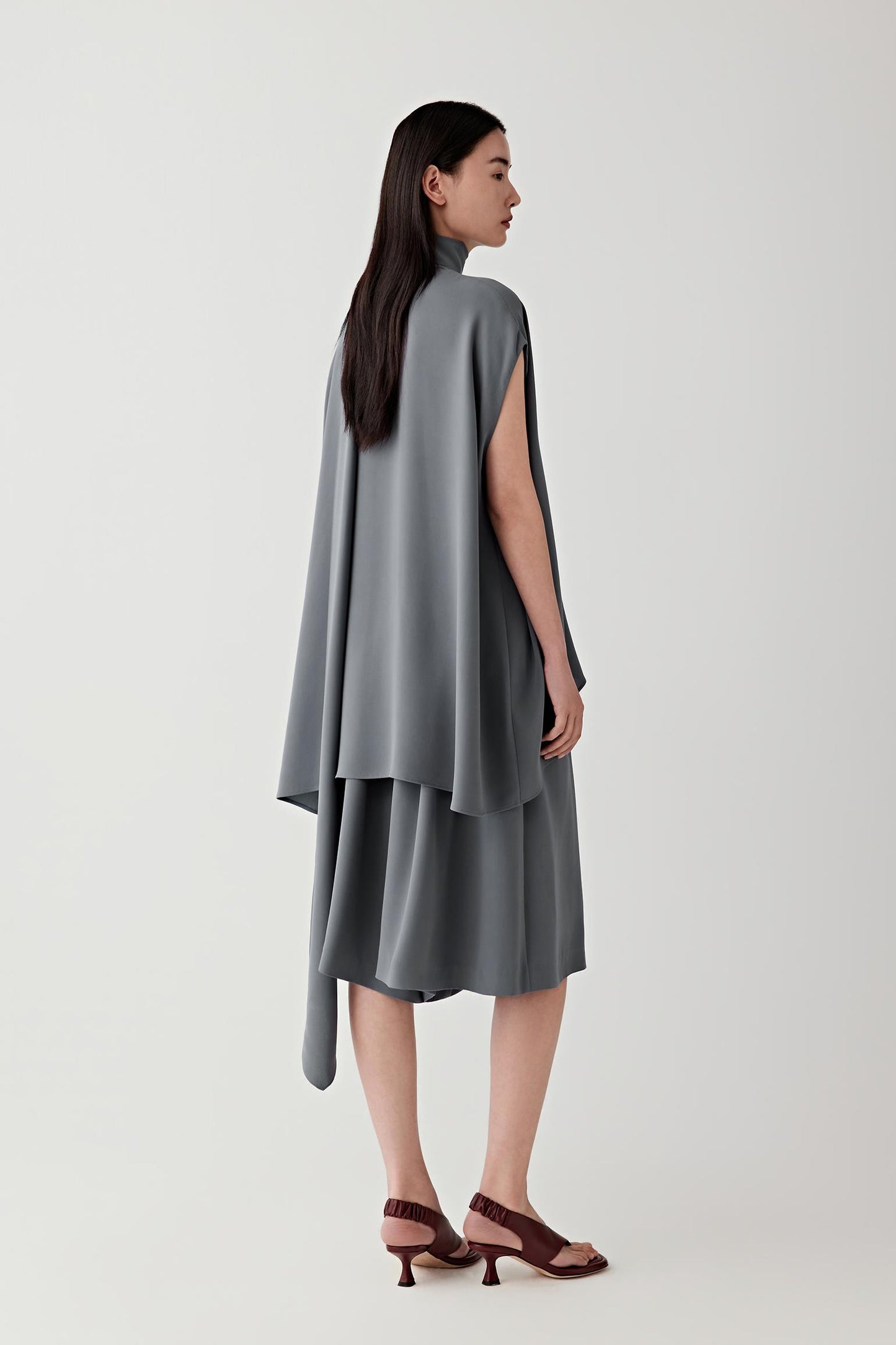 Side or three-quarter view emphasizing the layered construction and fluid drape of the heavy silk crepe. The fabric falls softly away from the body, revealing the continuous movement and balanced proportions of the silhouette.