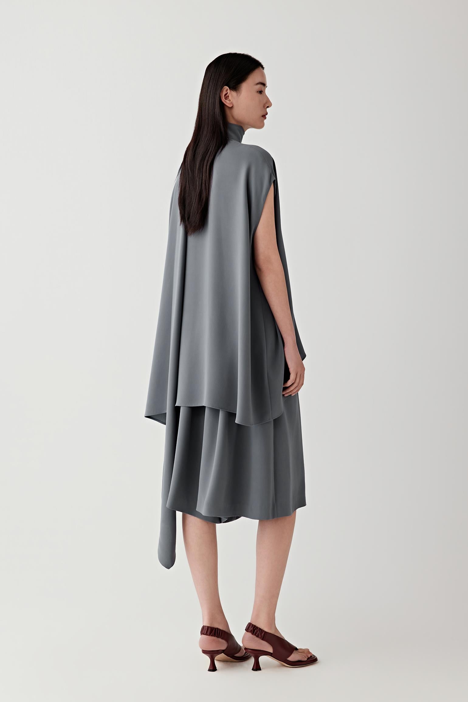 Side or three-quarter view emphasizing the layered construction and fluid drape of the heavy silk crepe. The fabric falls softly away from the body, revealing the continuous movement and balanced proportions of the silhouette.