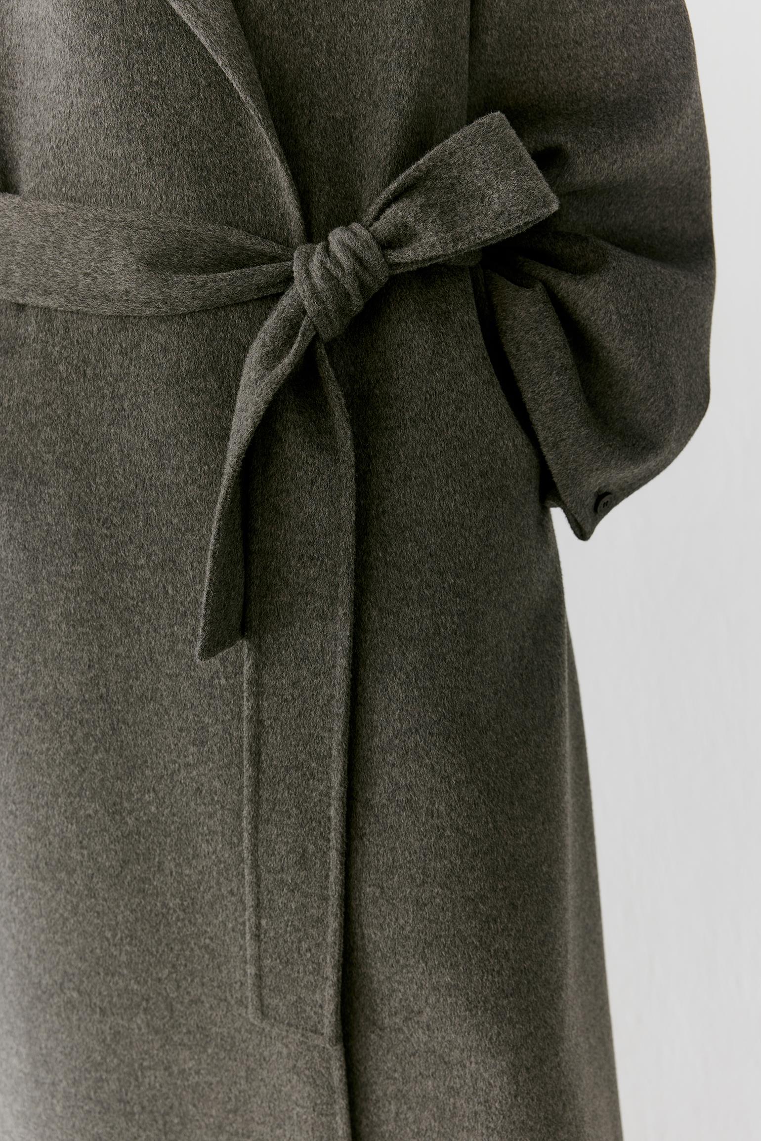 Close-up of a dark olive gray wool coat with a matching tie belt, showing the texture and fabric detail against a light gray background.