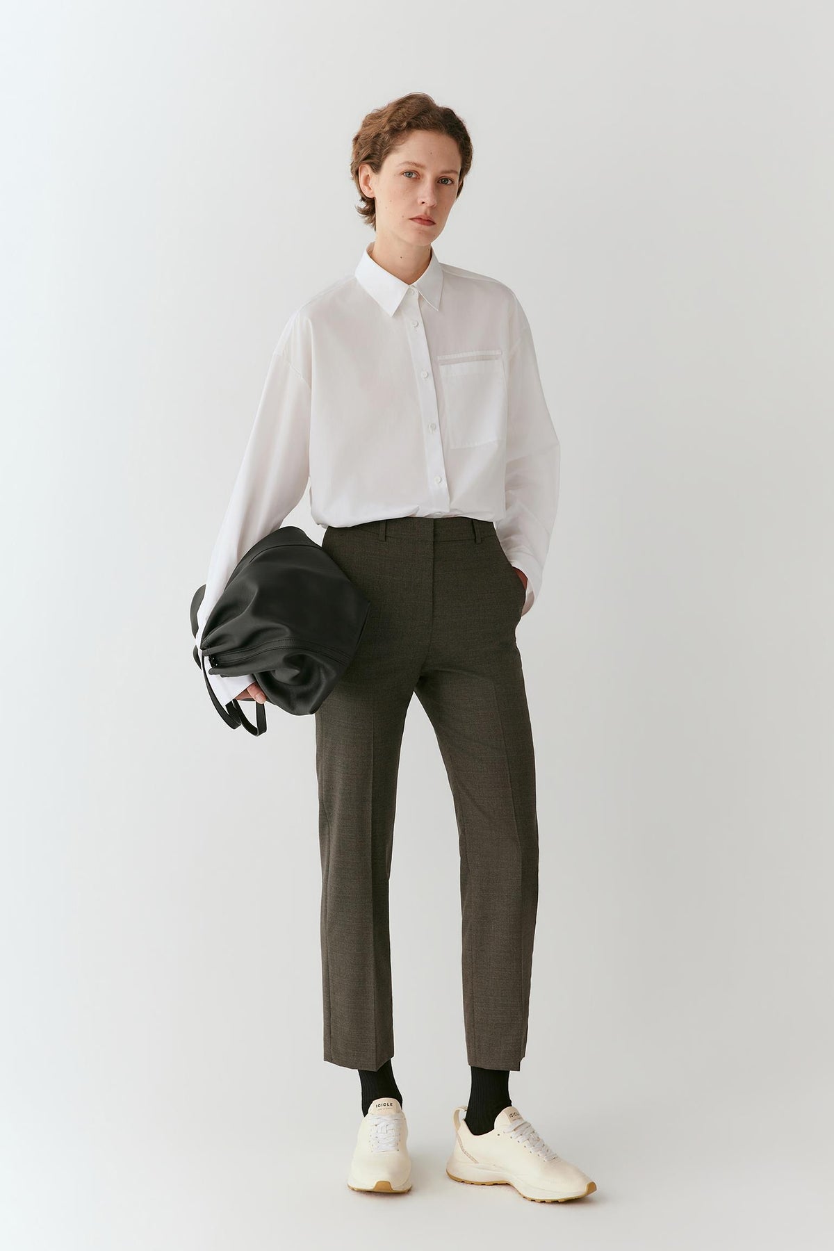 Front view of a woman wearing grey melange wool suiting trousers, highlighting the bootcut silhouette, pressed creases and structured drape.
