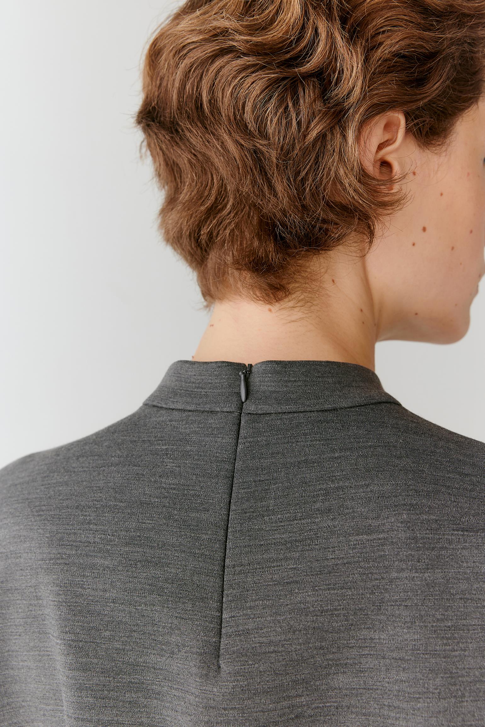 Close-up back view of a person with short wavy brown hair wearing a dark gray ribbed knit top or sweater, showing the center back zipper and collar.
