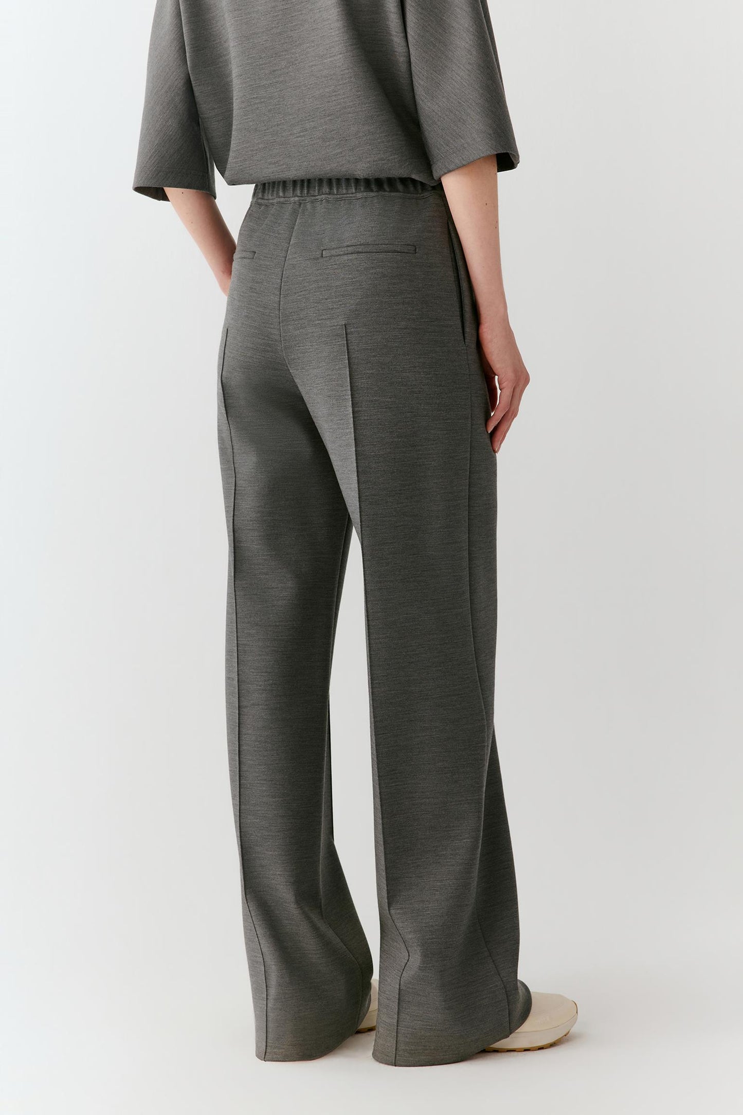 A model shown from the back wearing dark gray wide-leg trousers and a matching gray top, photographed against a clean light gray studio background.