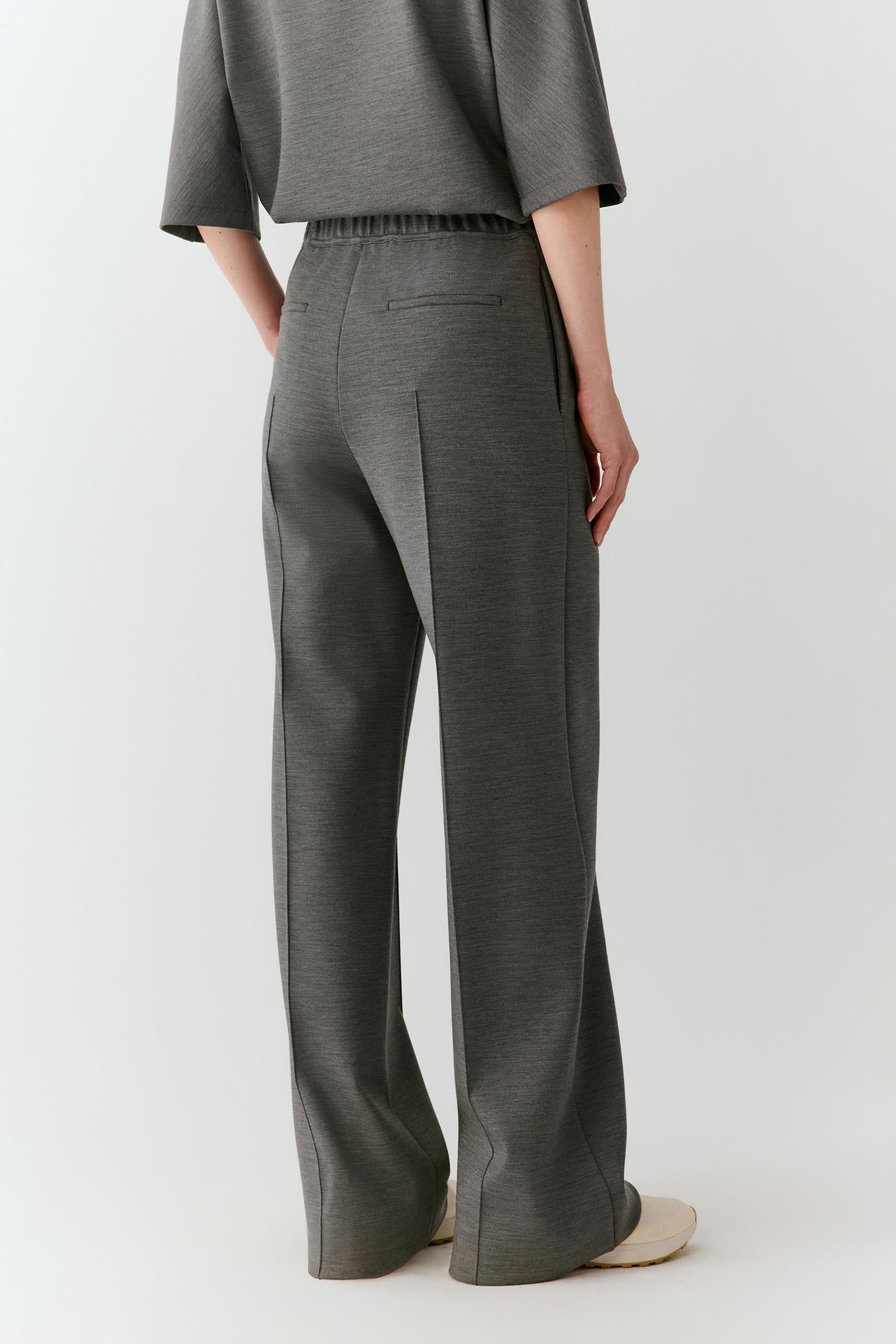 A model shown from the back wearing dark gray wide-leg trousers and a matching gray top, photographed against a clean light gray studio background.
