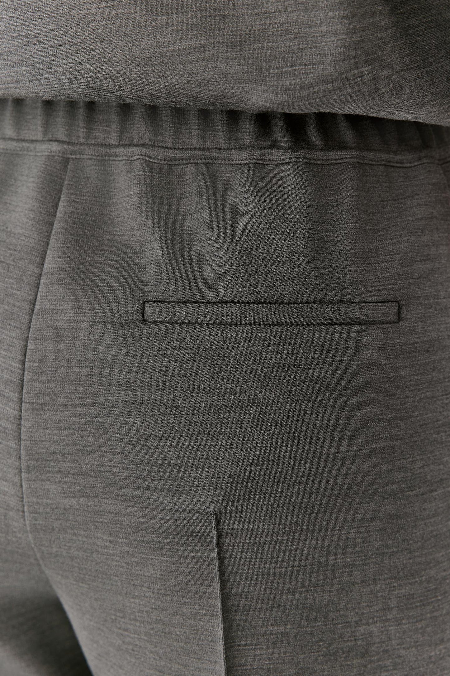 Close-up of dark gray heathered fabric clothing showing an elastic waistband, a horizontal welt pocket, and a vertical seam.