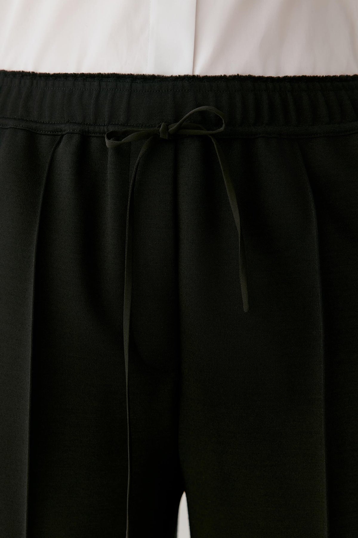 Close-up of black drawstring trousers with a wide elastic waistband, shown against a white top.
