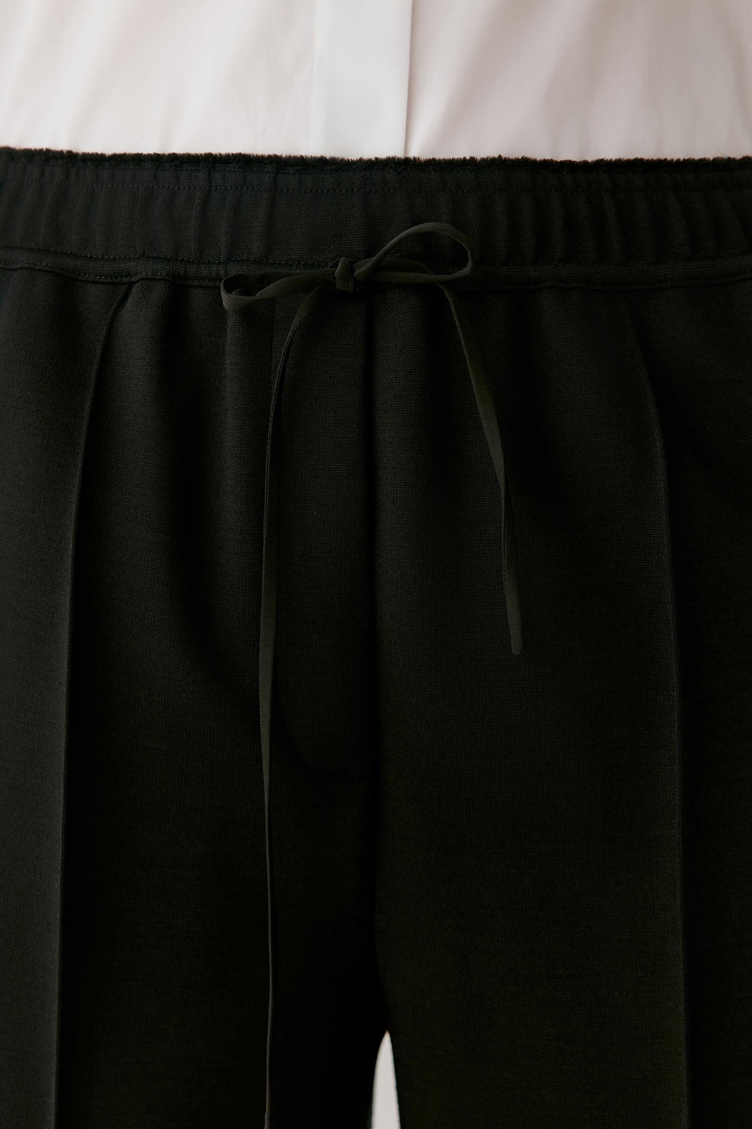 Close-up of black drawstring trousers with a wide elastic waistband, shown against a white top.