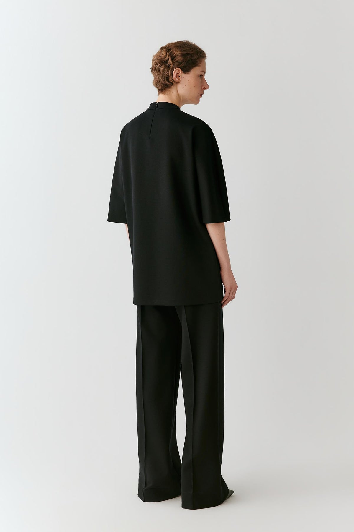 A model shown from the back wearing a black short-sleeved top and matching wide-leg trousers against a light gray studio background.