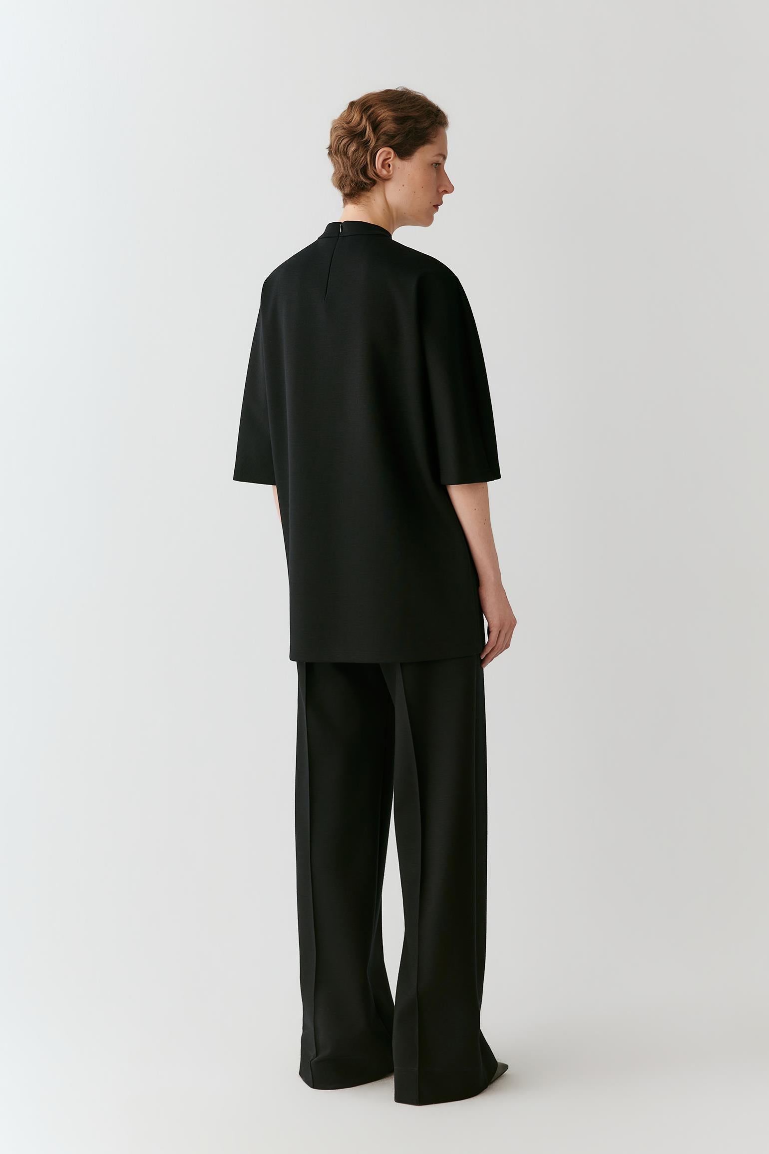 A model shown from the back wearing a black short-sleeved top and matching wide-leg trousers against a light gray studio background.
