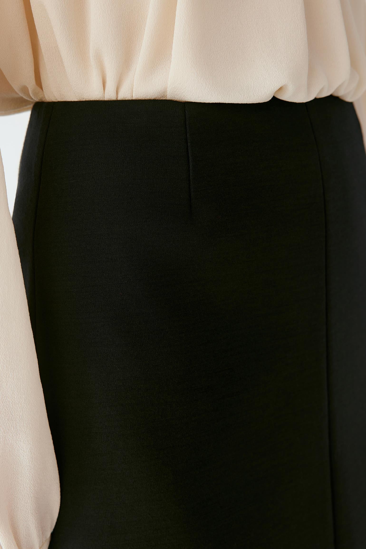 Close-up of a black skirt with a front center seam, paired with a cream-colored blouse.