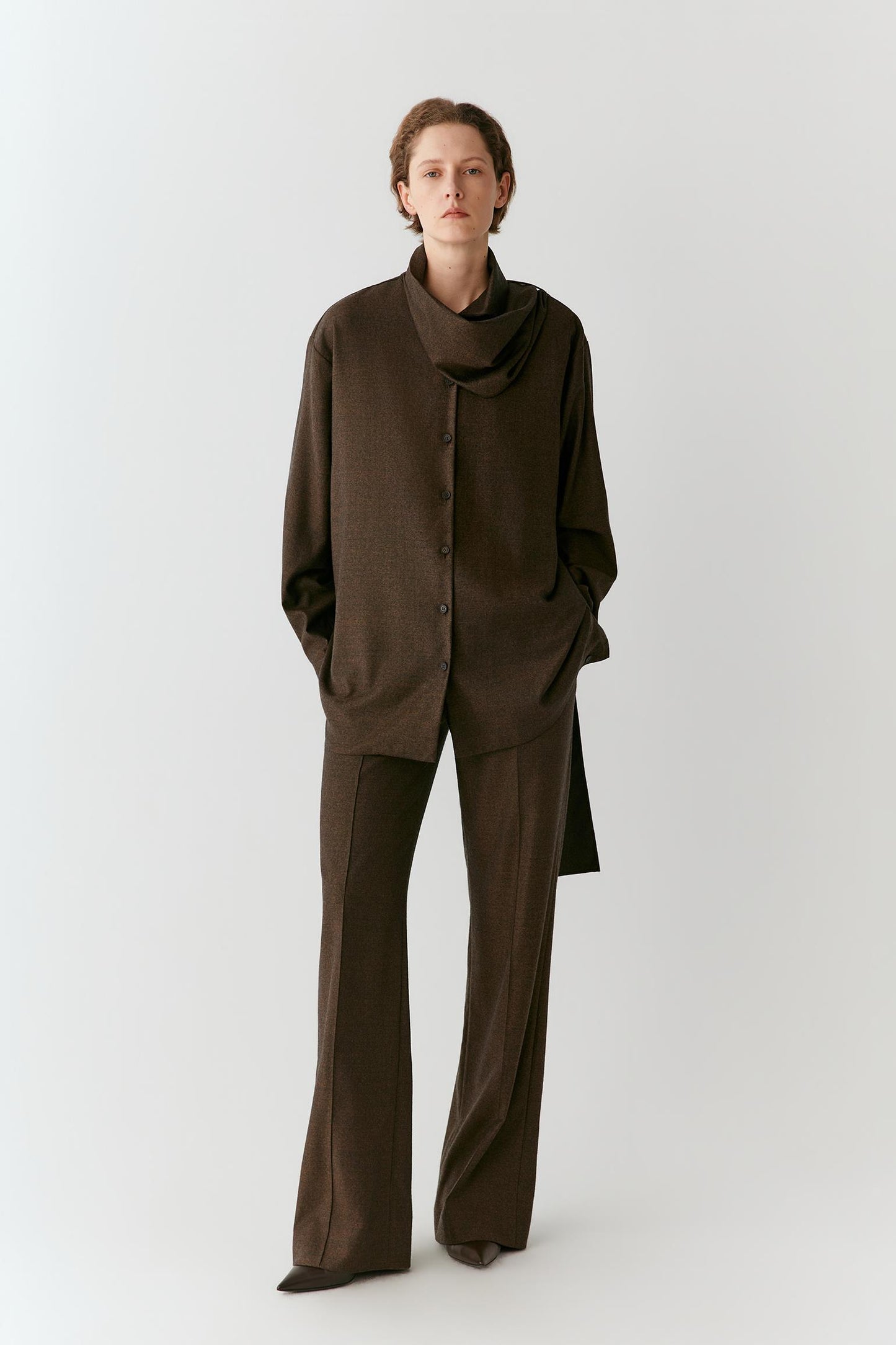 Front view of a woman wearing brown melange wool flannel trousers, showing the straight-leg silhouette and fluid drape.