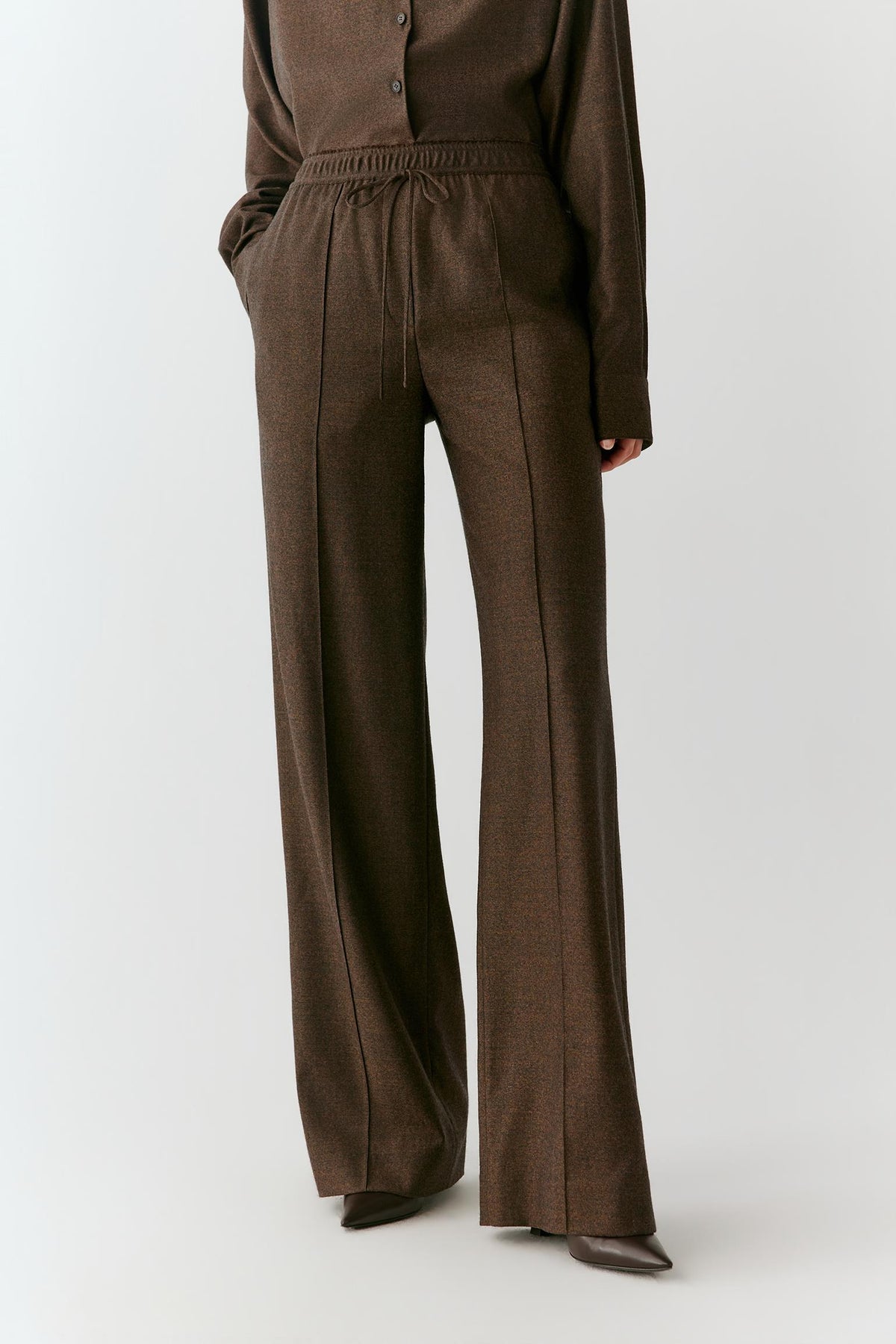 Front view highlighting the straight-leg cut, pressed seams and relaxed drape of the brown wool flannel trousers.