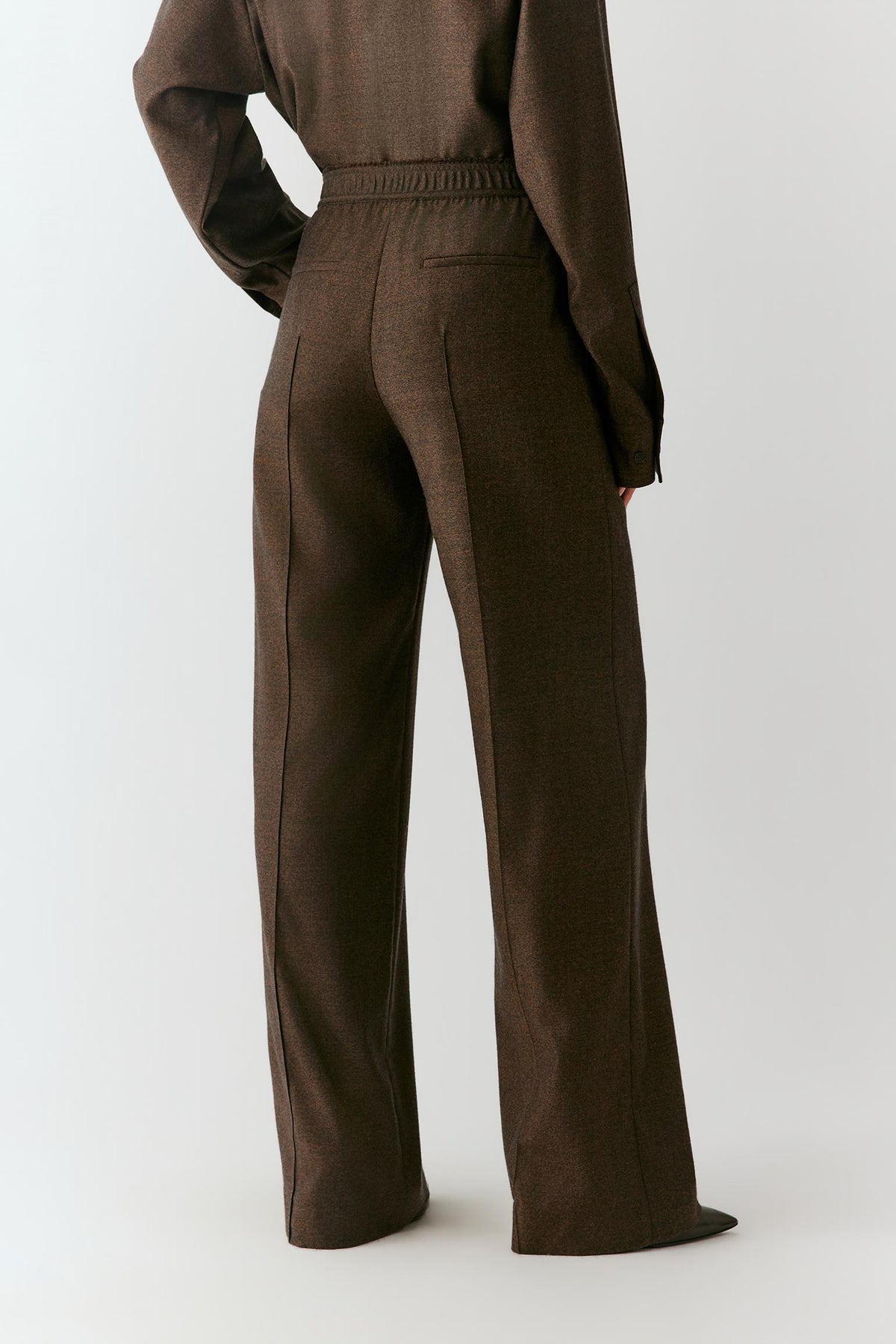 Three-quarter view showing the straight-leg silhouette and fluid drape of the brown wool flannel trousers.