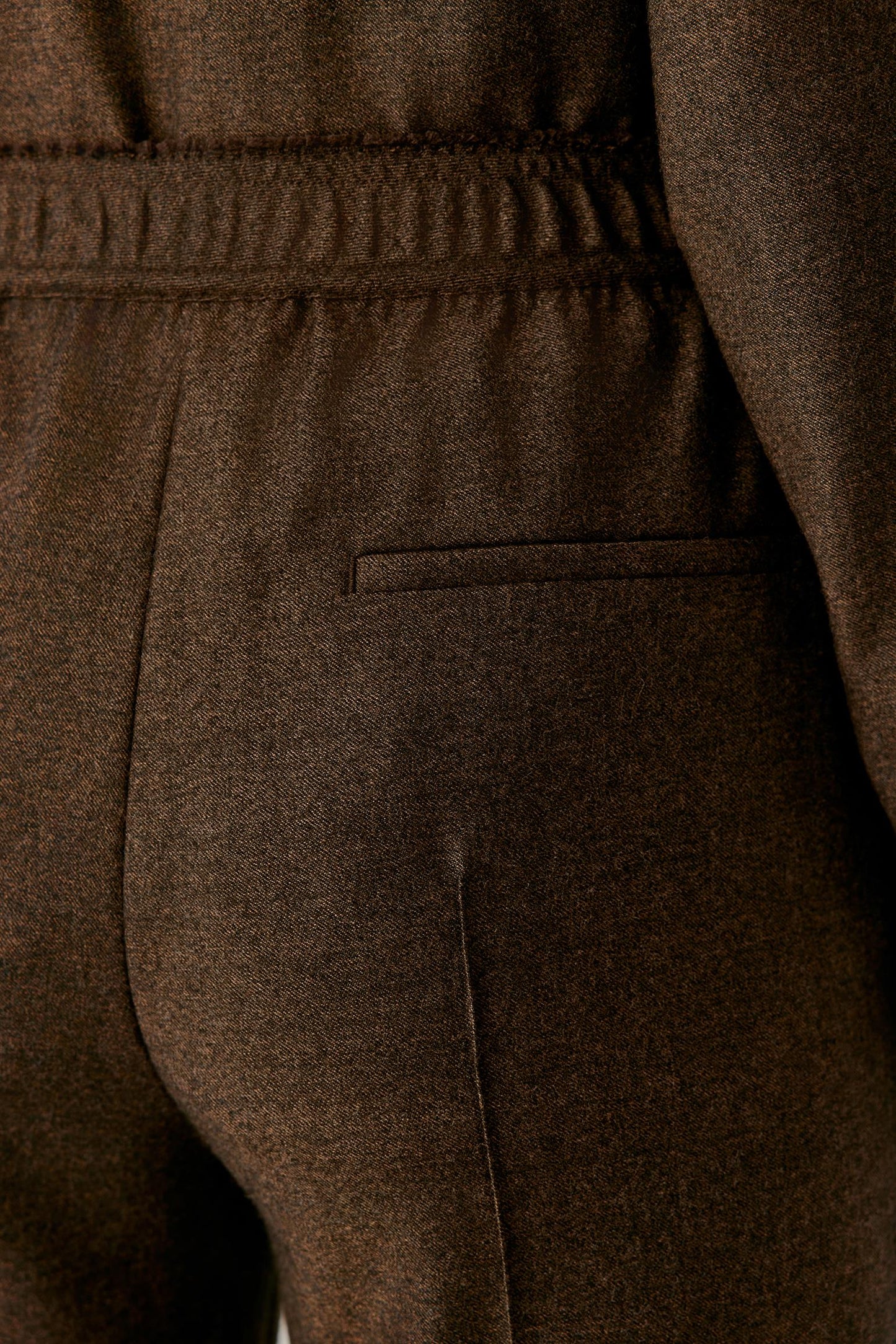 Close-up of the waistband and rear welt pocket of the brown wool flannel trousers.