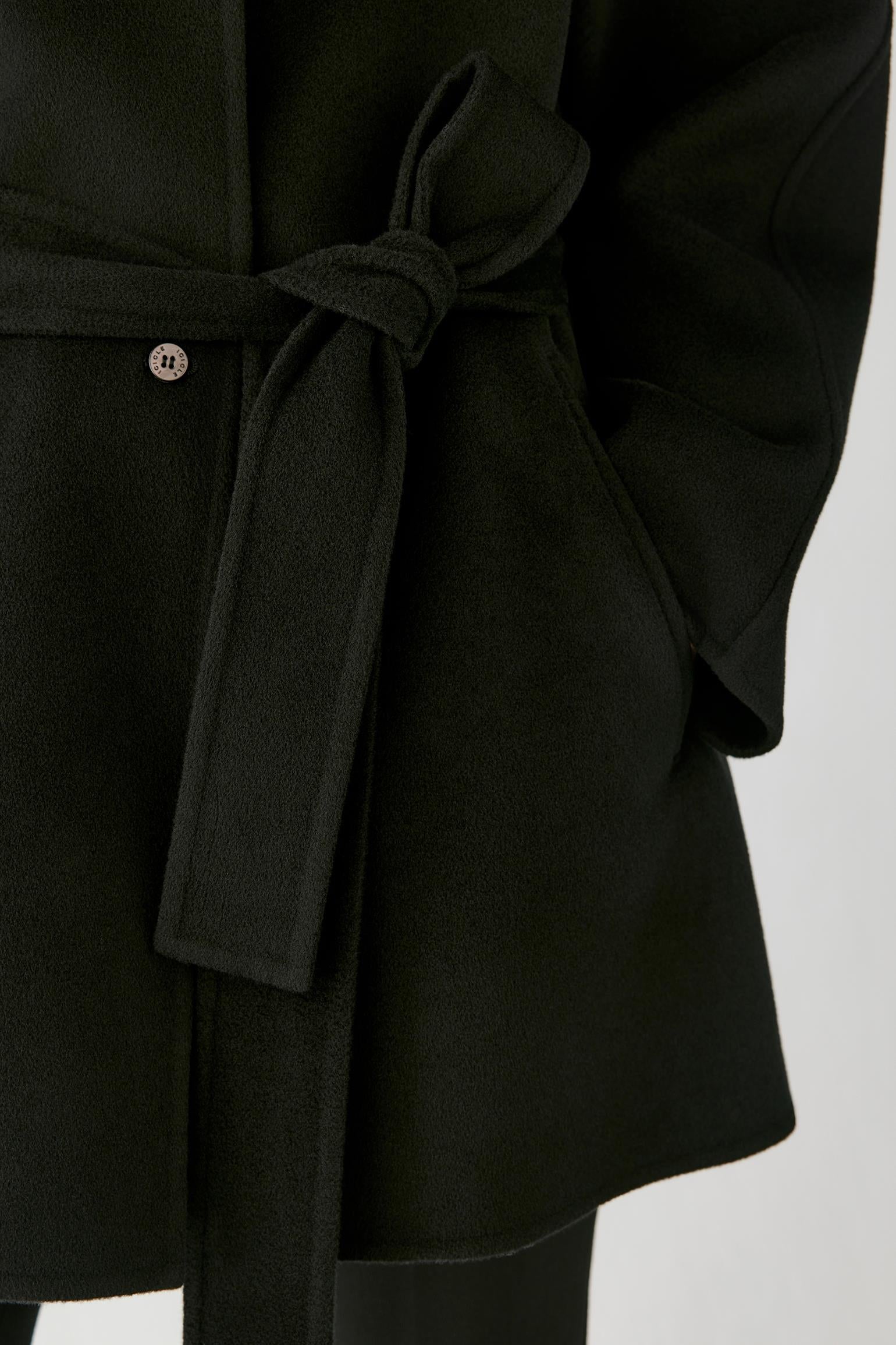 Close-up of a black belted coat with a matching tie belt and a small metallic button detail, shown against a light gray background.