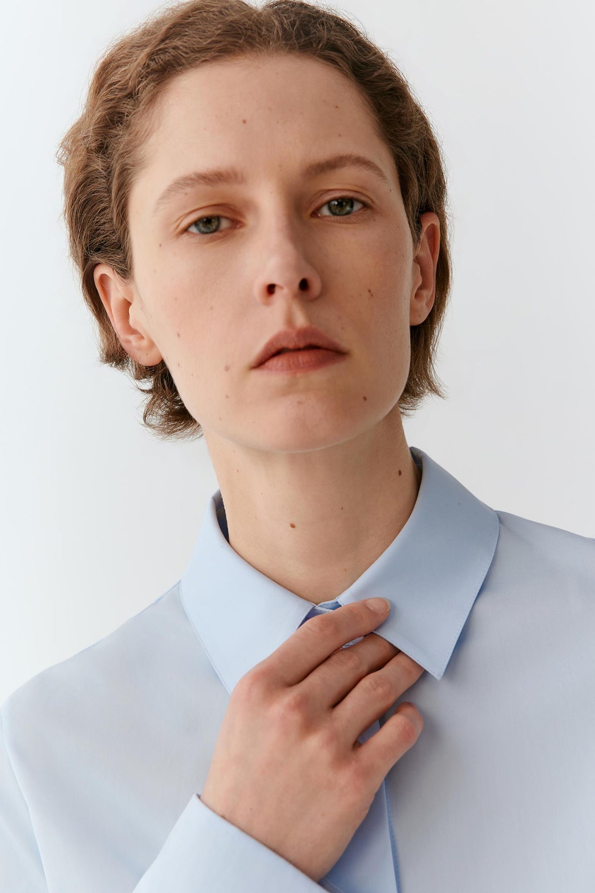 A close-up portrait of a model wearing a light blue dress shirt and matching tie against a plain light gray background.