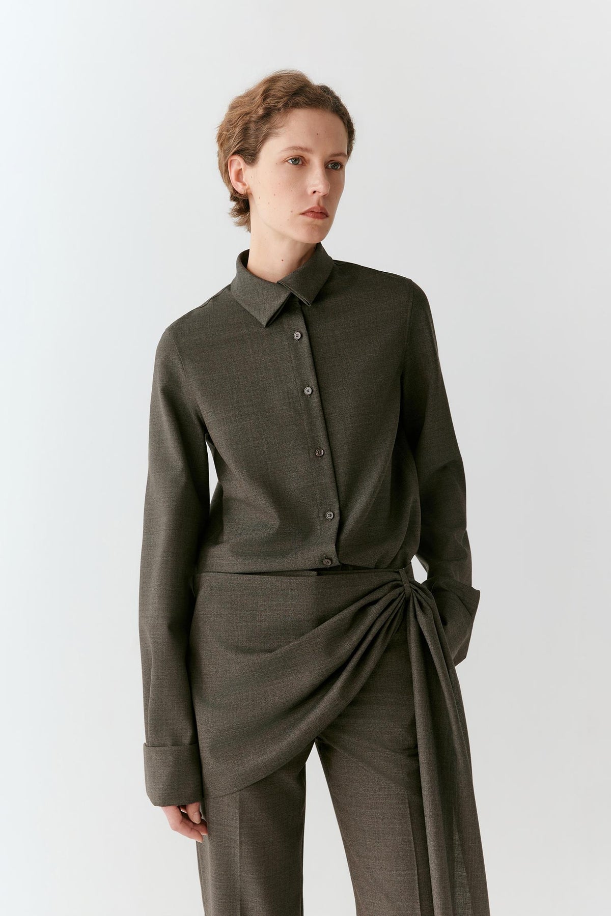 Front view of a woman wearing a medium grey melange wool suiting shirt, highlighting the straight hem, pointed collar and concealed fastening.