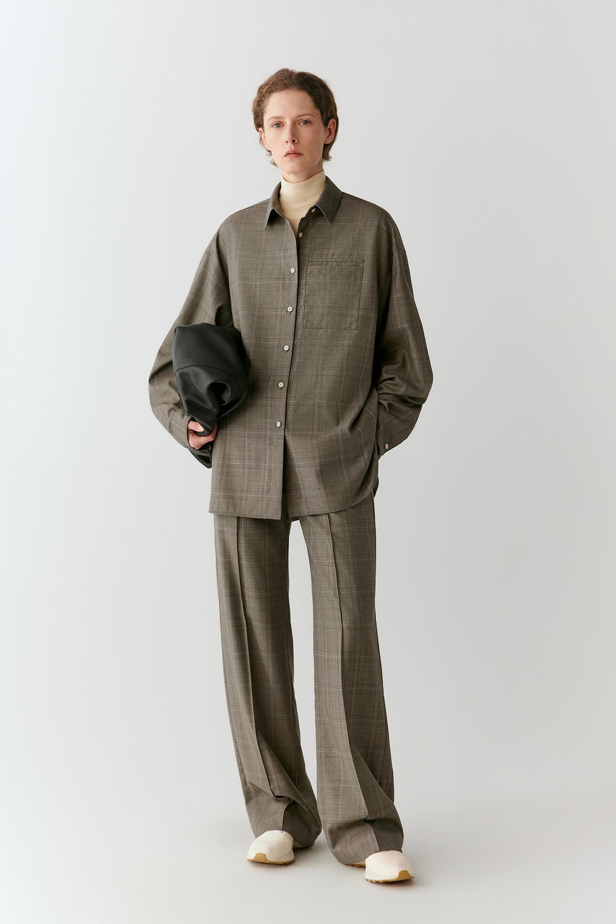 Front view of a woman wearing taupe and grey Glen plaid trousers, highlighting the straight-leg silhouette and pressed creases.