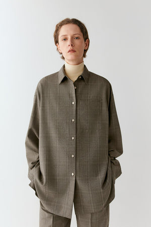 Front view of a woman wearing a grey checked Glen plaid wool shirt, showing the relaxed silhouette and pointed collar.