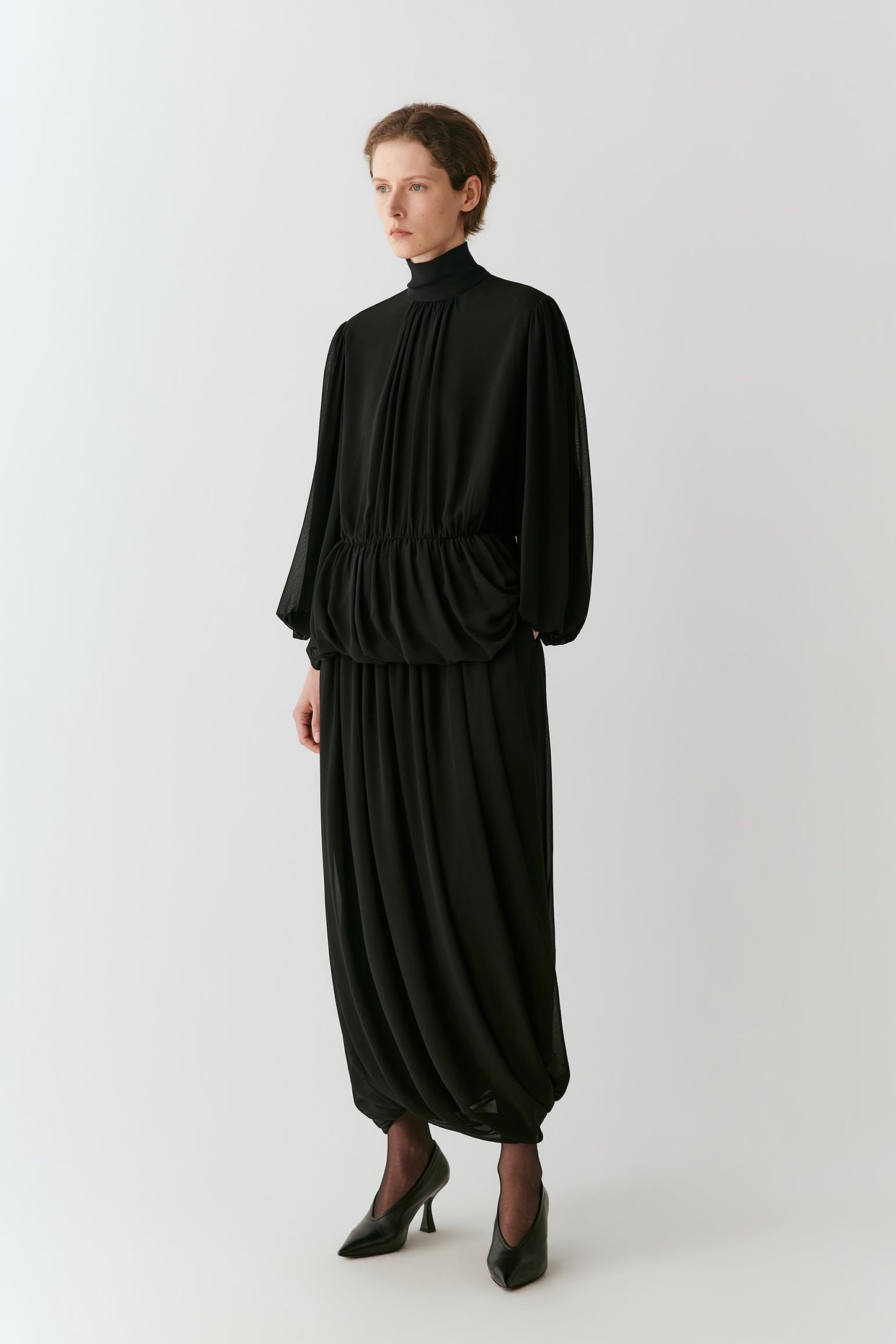 Front view of a woman wearing a deep black silk georgette long skirt, highlighting the gathered volume and rounded silhouette.