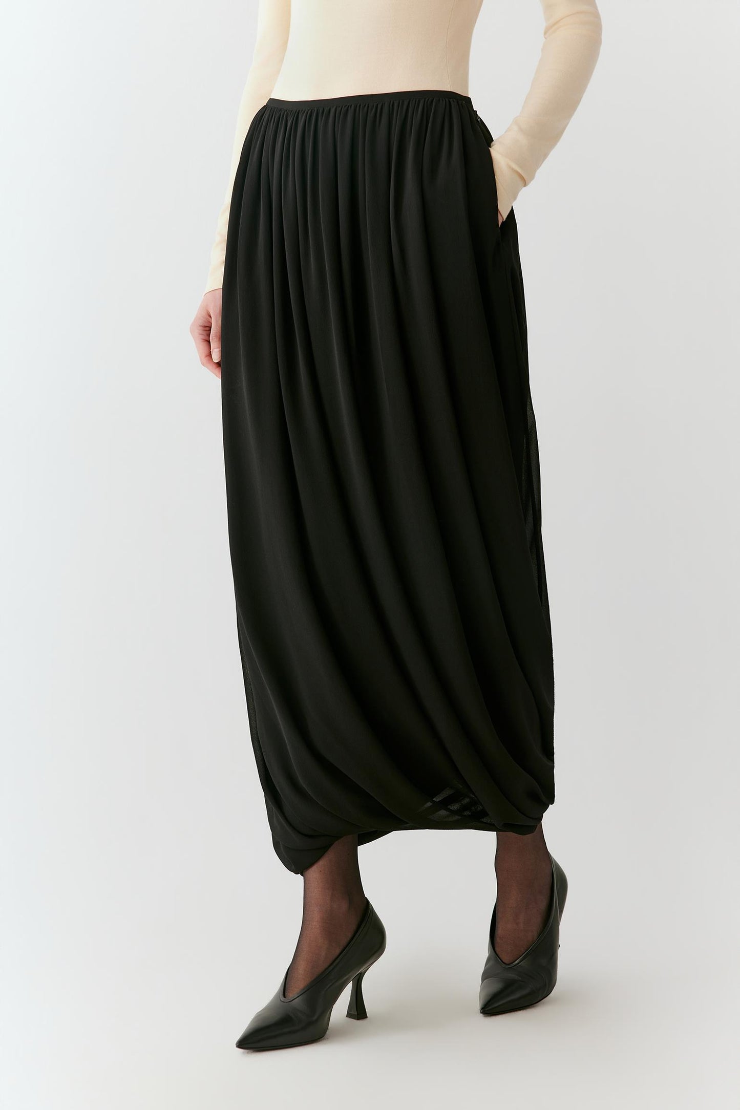 Three-quarter view highlighting the fluid drape and rounded hem of the black silk skirt.