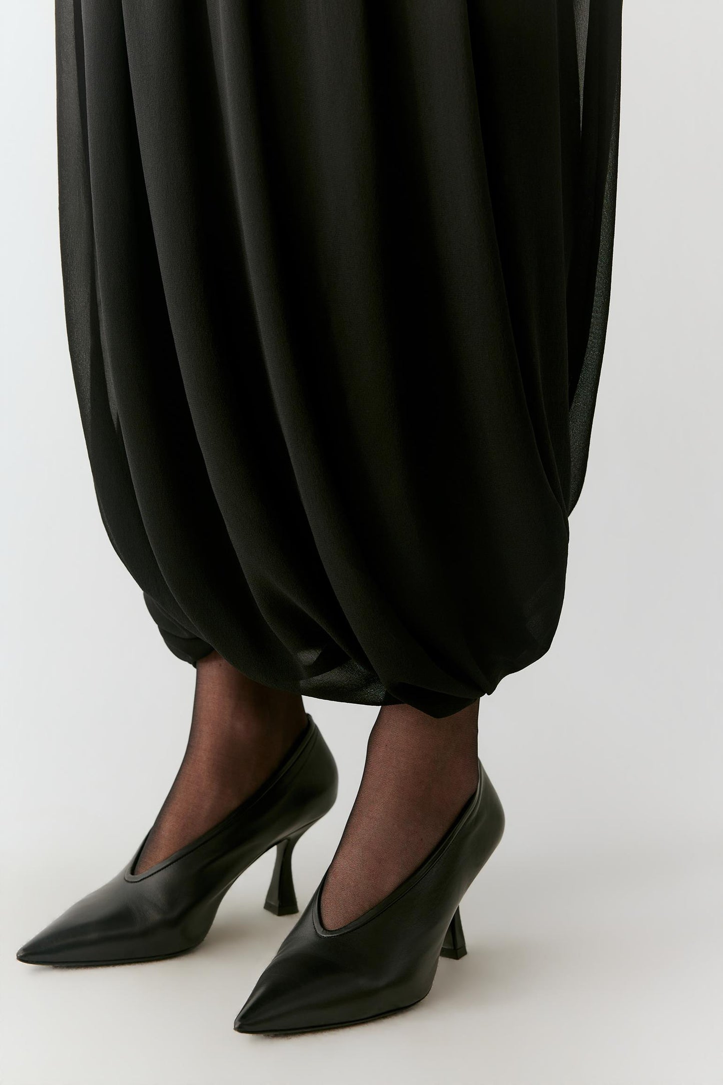 Close-up of the rounded hem, highlighting the gathered volume and fluid drape of the black silk skirt.