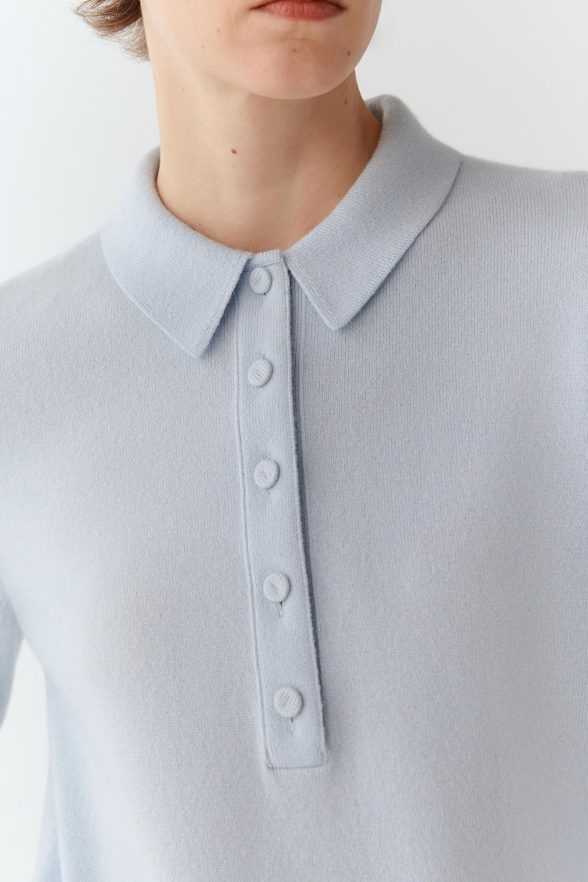 Close-up of a person wearing a light blue knit polo sweater with a collar and three-button placket.