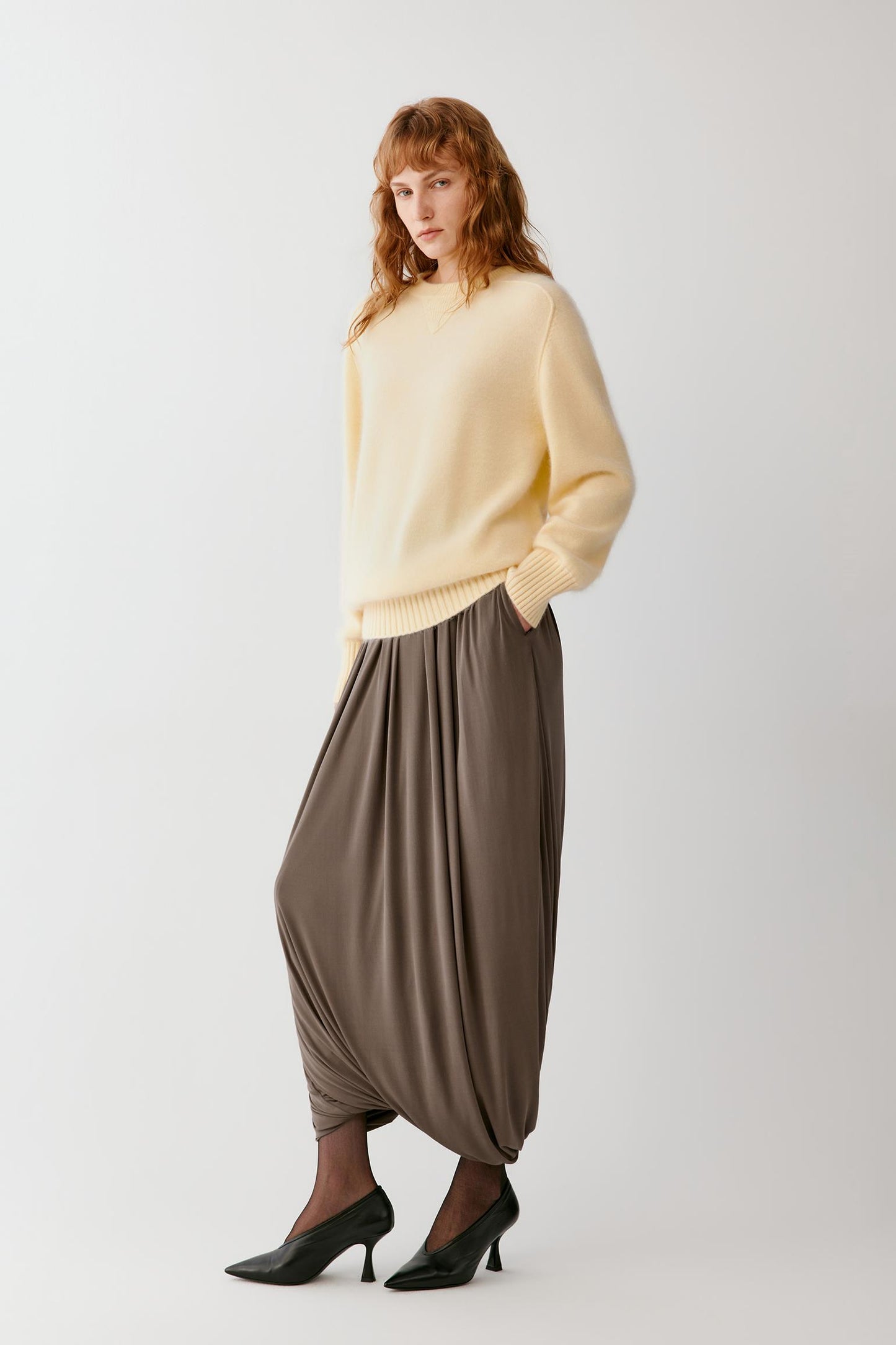 Front view of a woman wearing a taupe silk jersey skirt, highlighting the long cocoon silhouette, gathered volume and fluid drape.