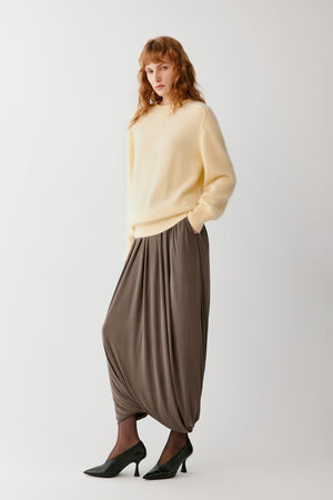 Front view of a woman wearing a taupe silk jersey skirt, highlighting the long cocoon silhouette, gathered volume and fluid drape.