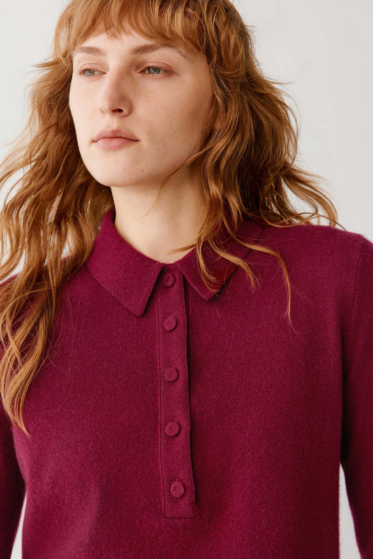A close-up of a woman wearing a long-sleeve knit polo shirt in a deep burgundy or maroon color, featuring a classic collar and a buttoned placket.