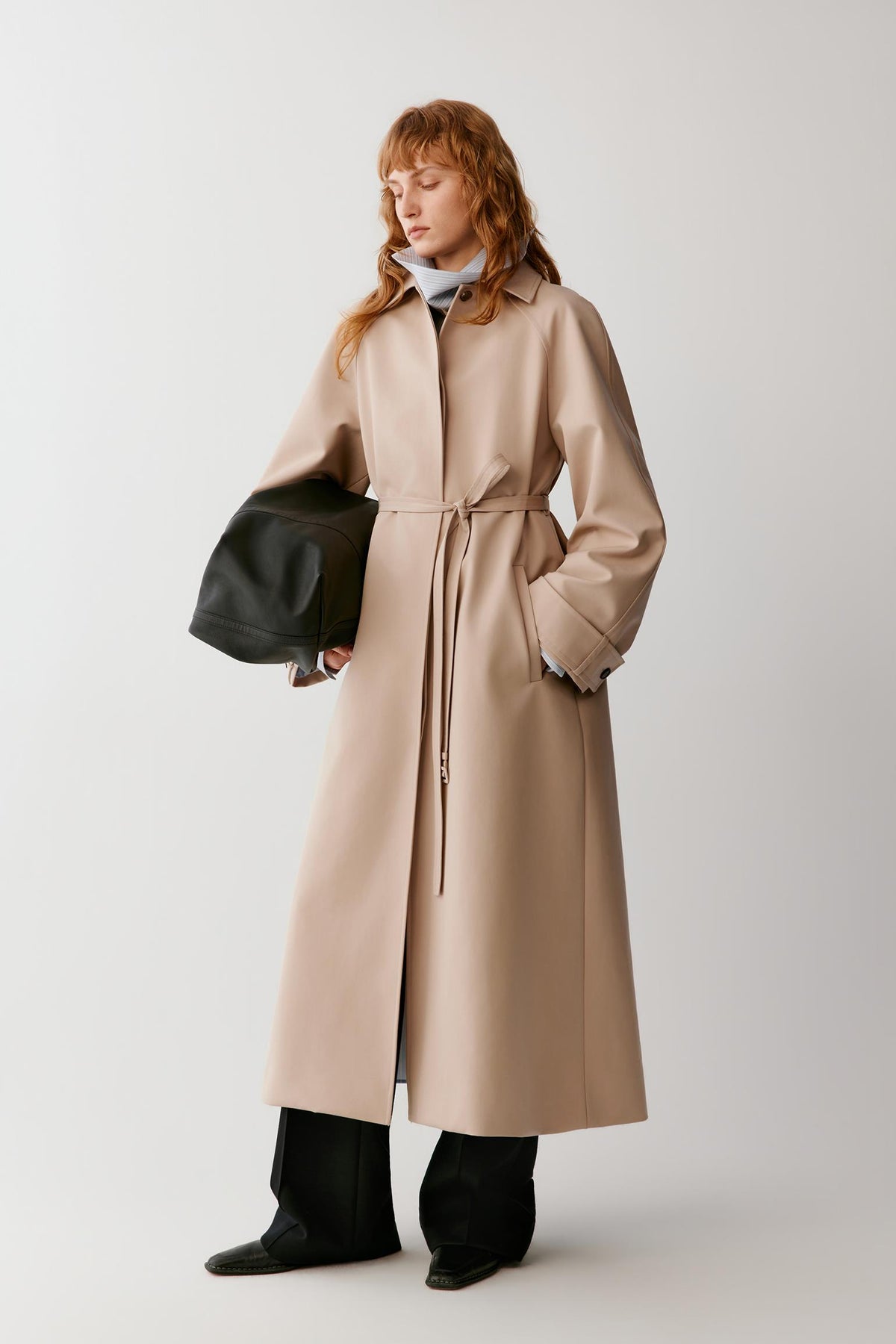 Front view of a woman wearing a beige wool and silk trench coat, highlighting the long silhouette, raglan sleeves and adjustable waist belt.