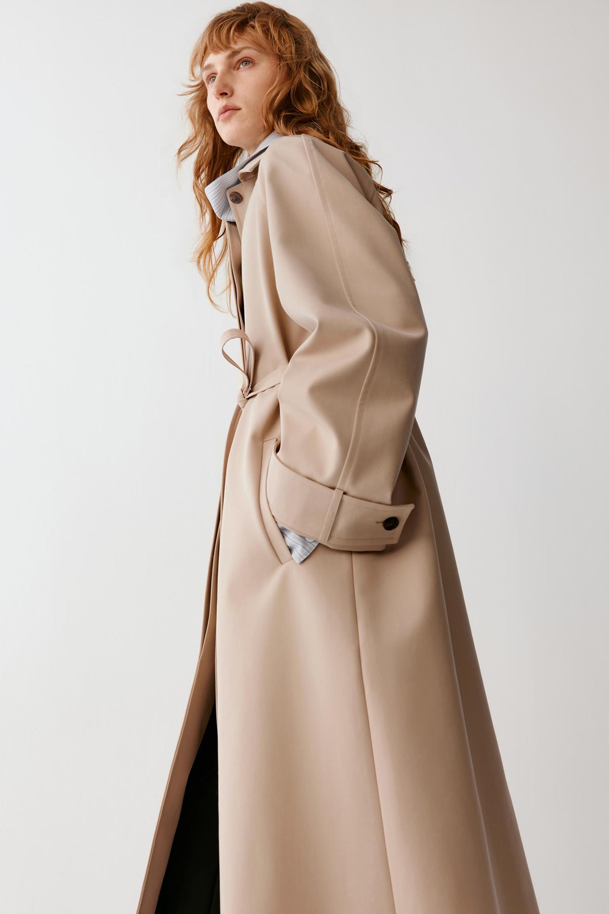 Three-quarter view showing the belted waist, wide cuffs and structured drape of the beige wool and silk fabric.